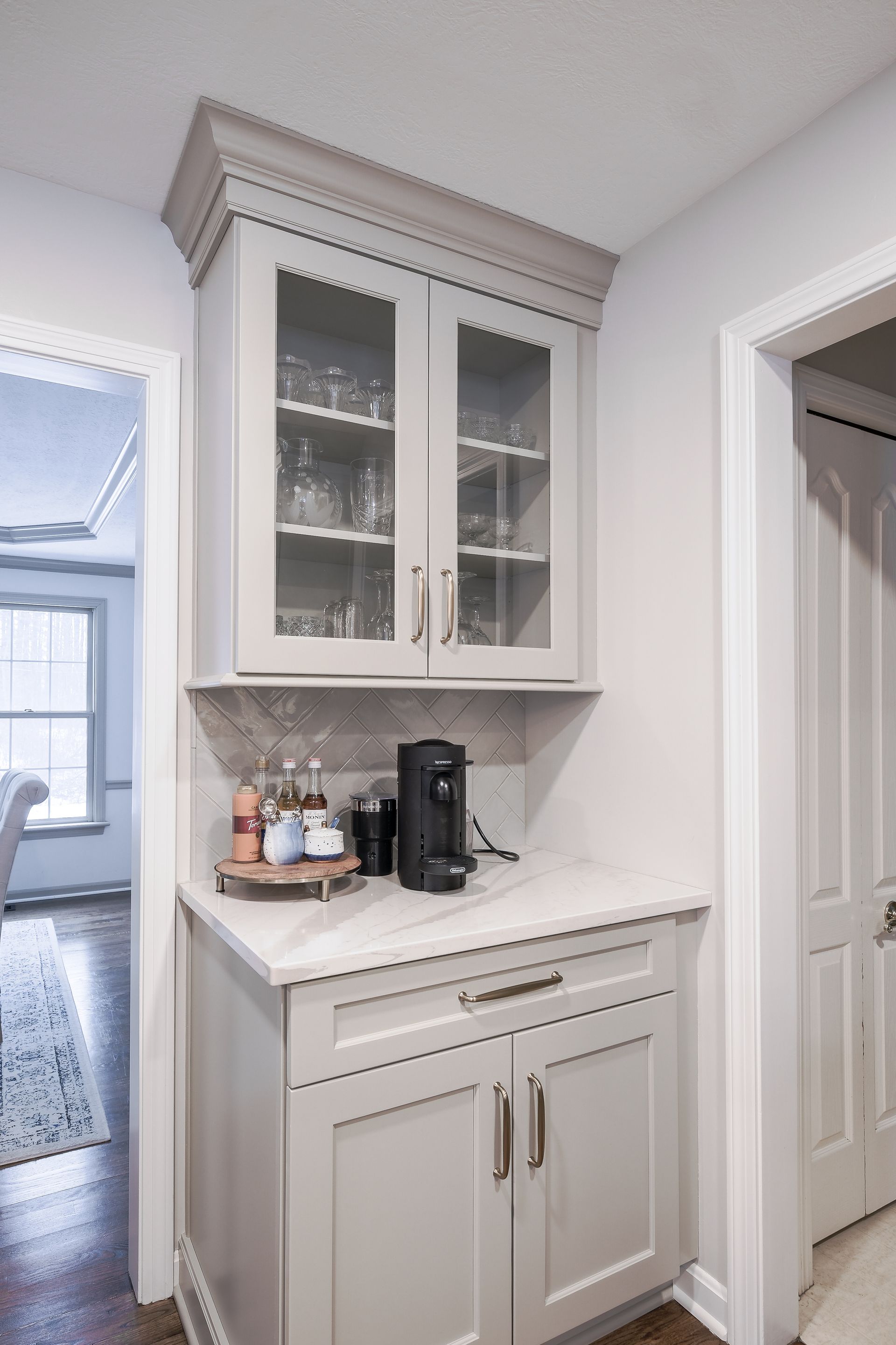 Light gray built-in kitchen cabinet with glass-door upper cabinets and a coffee station.