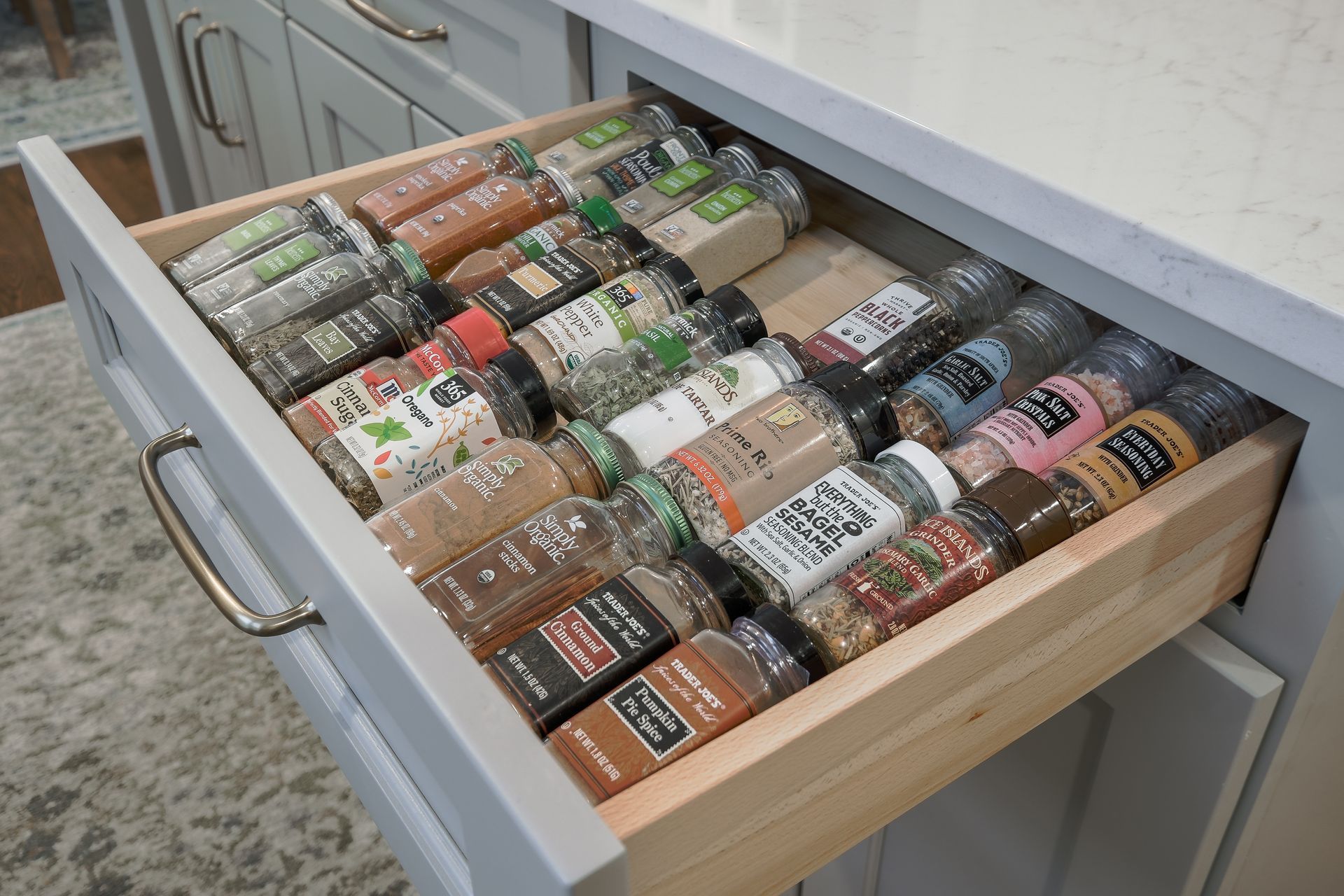 Drawer of spices in a kitchen cabinet, filled with various spice jars, organized and accessible.