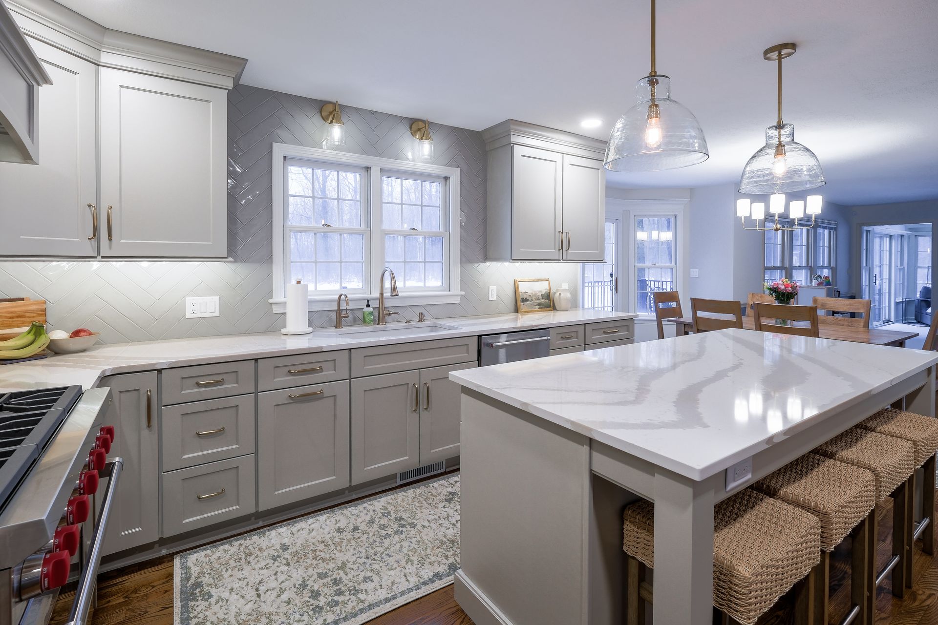 Modern kitchen with gray cabinets, marble countertops, island with seating, and pendant lights.