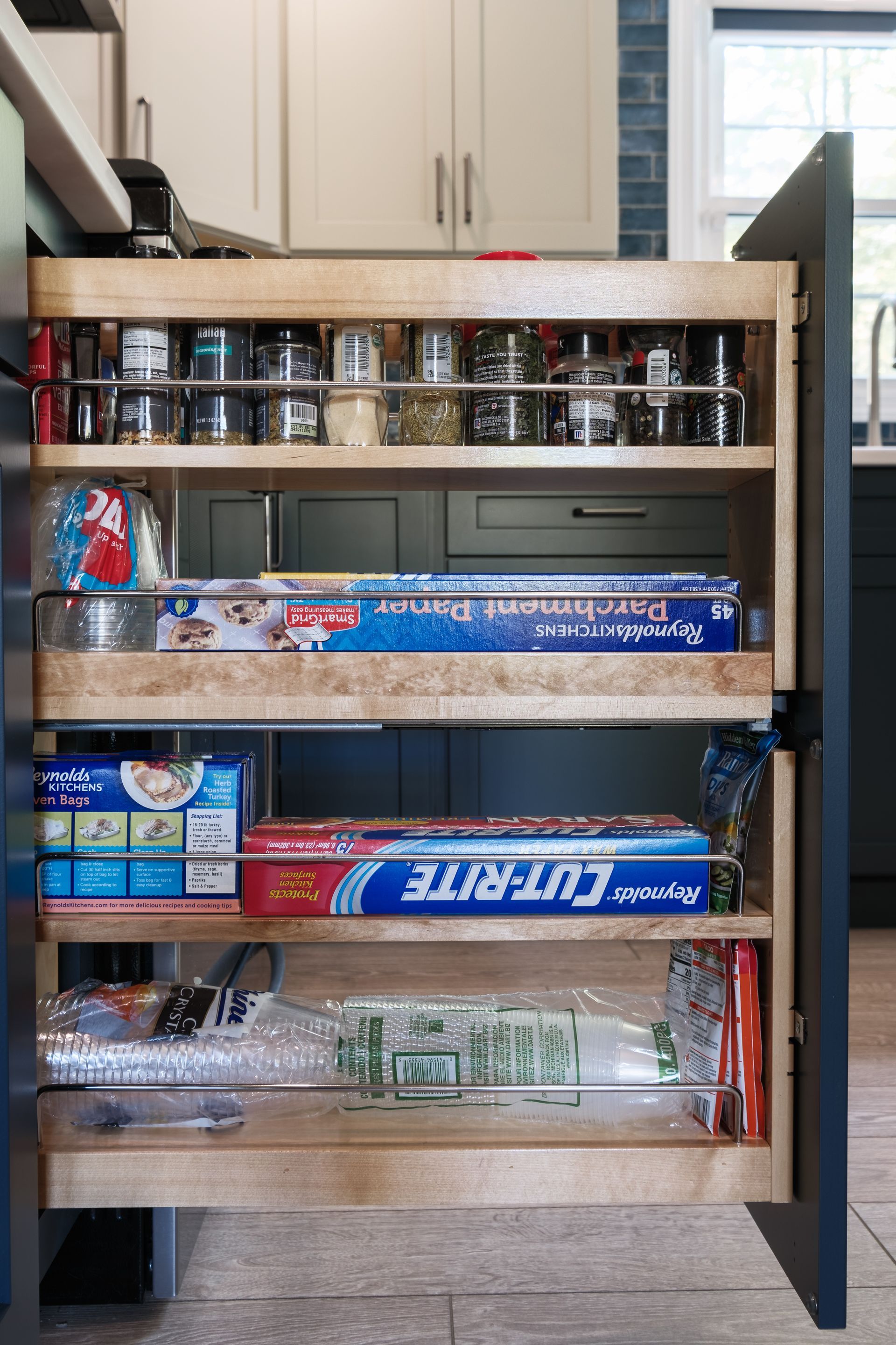A kitchen cabinet with a pull out drawer filled with various items.