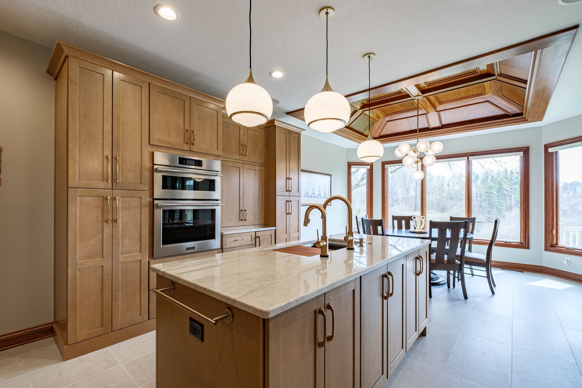 Modern kitchen with light wood cabinets, island, and dining area with large windows.