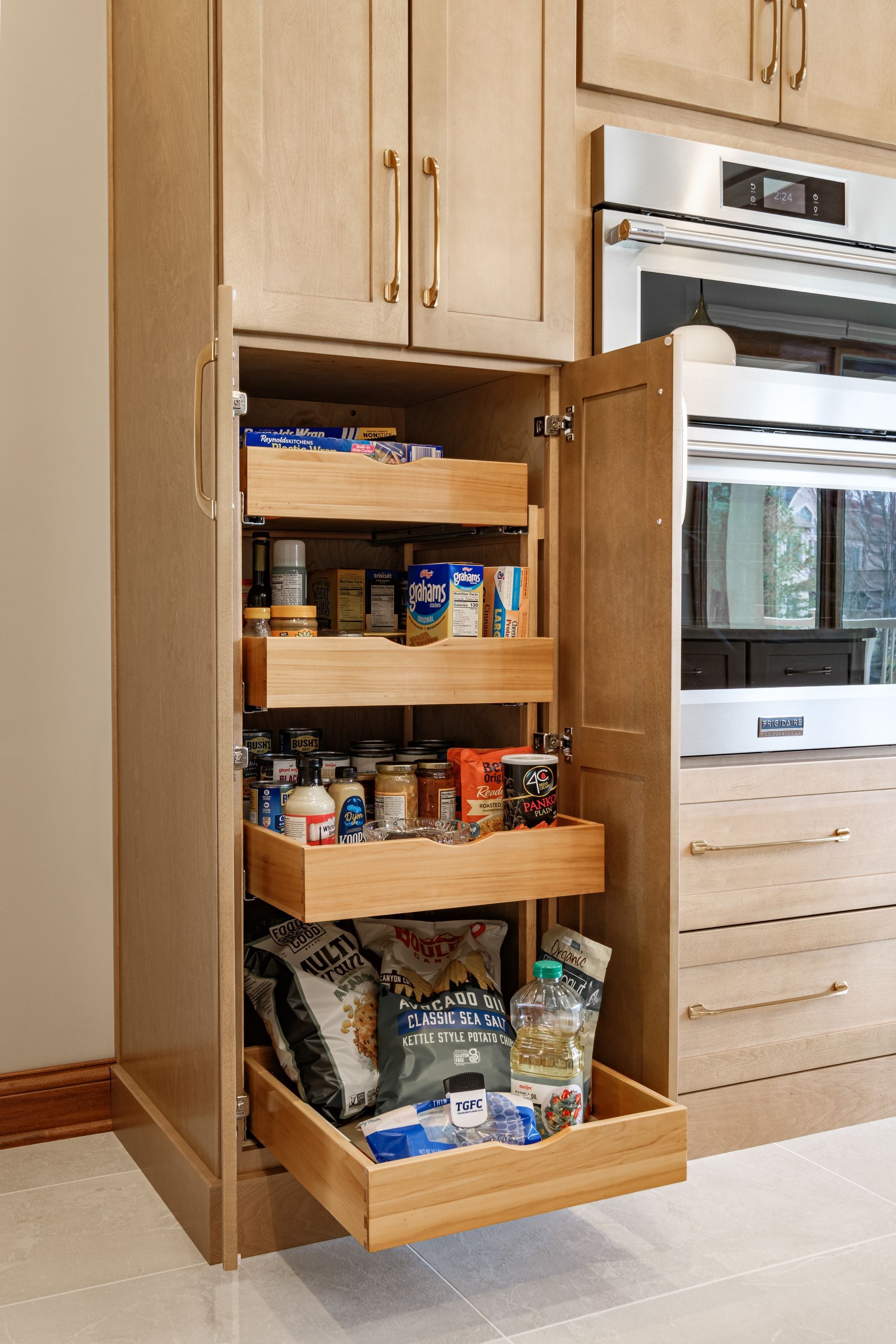Tall kitchen pantry with pull-out drawers, filled with food items, next to a stainless steel oven.
