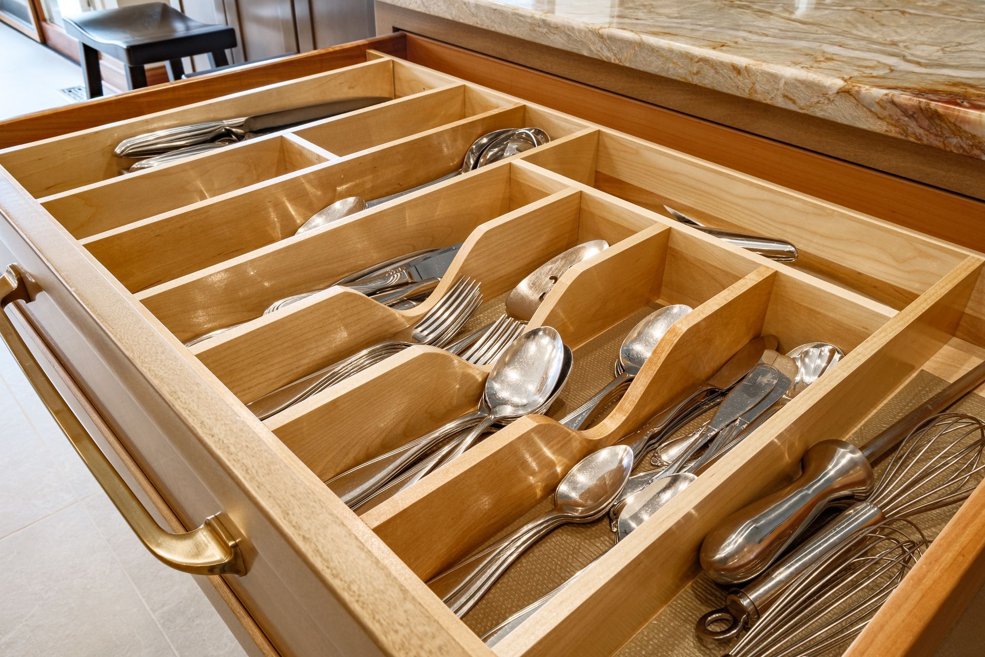 Open wooden kitchen drawer with silverware and a whisk in separated compartments.
