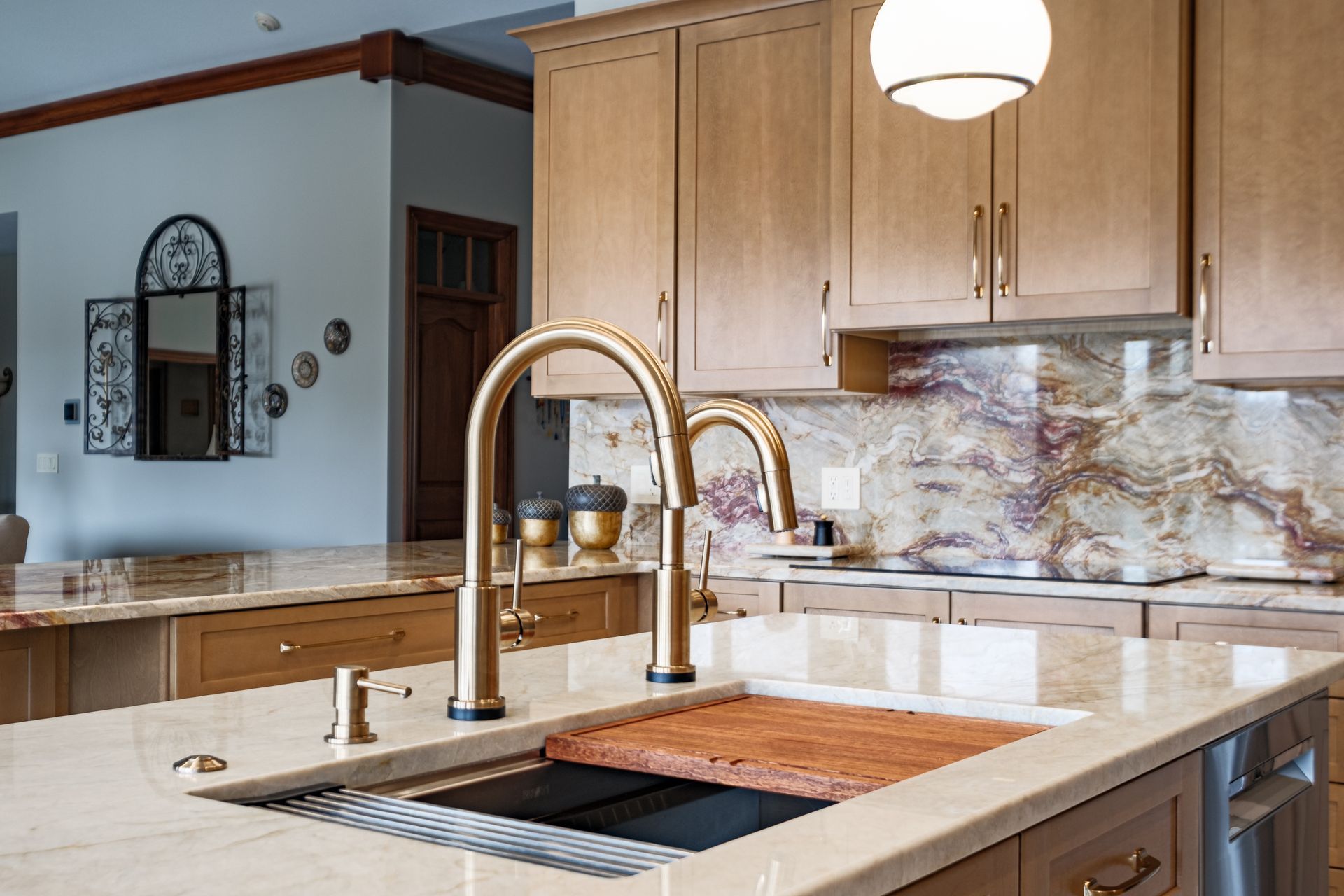 Kitchen island with gold faucet, sink, wooden cutting board, light cabinets, and marble backsplash.