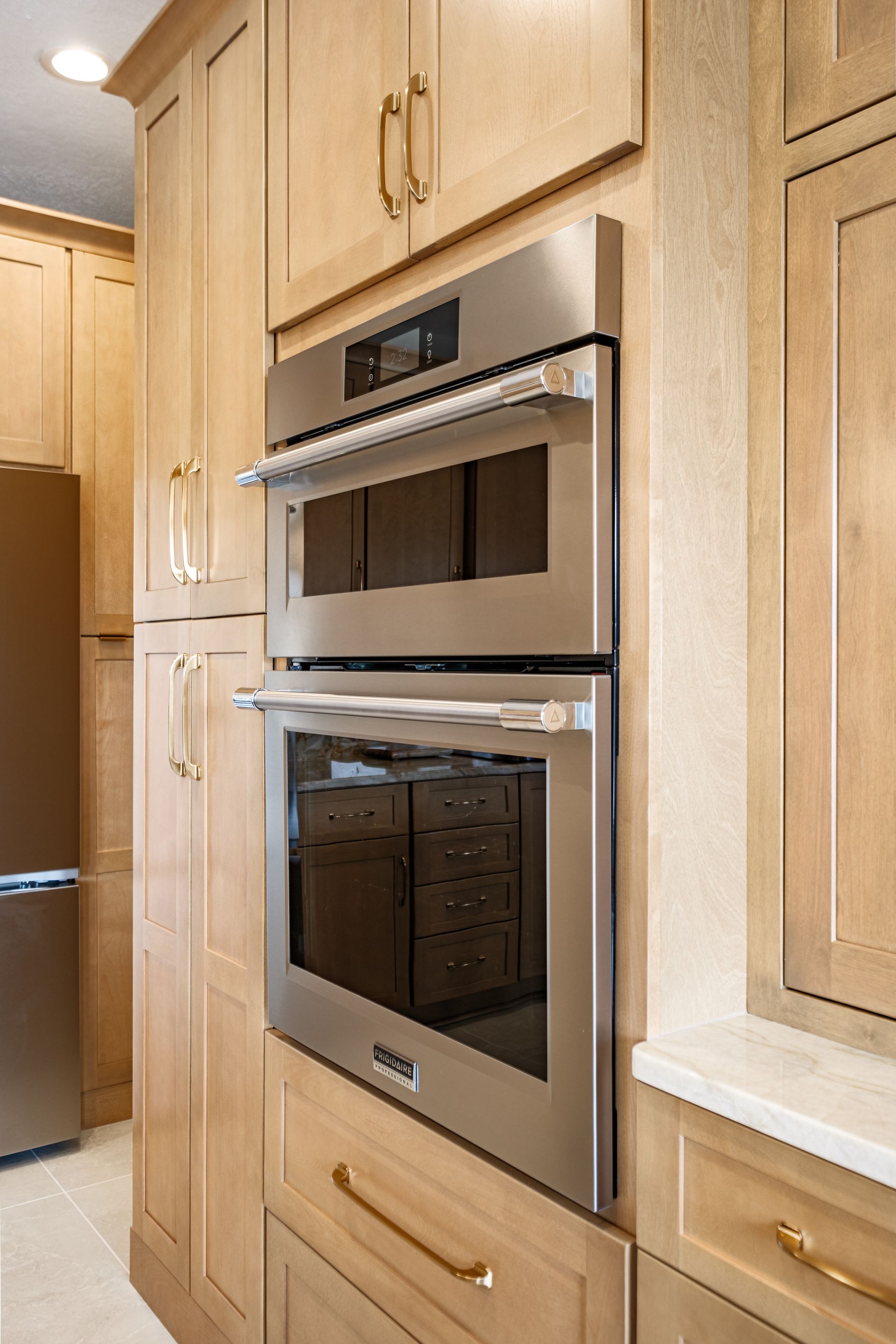 Stainless steel oven and microwave built into light wood cabinetry in a kitchen.