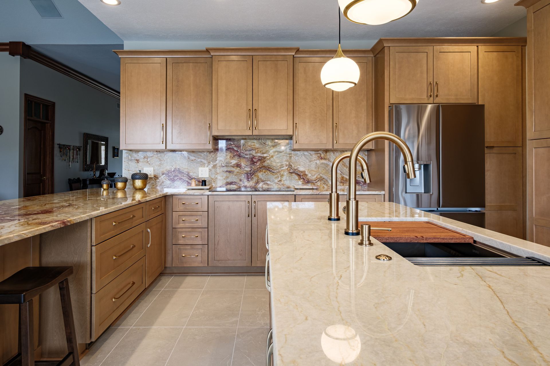 A modern kitchen with light-colored cabinets, marble countertops, stainless steel appliances, and gold fixtures.