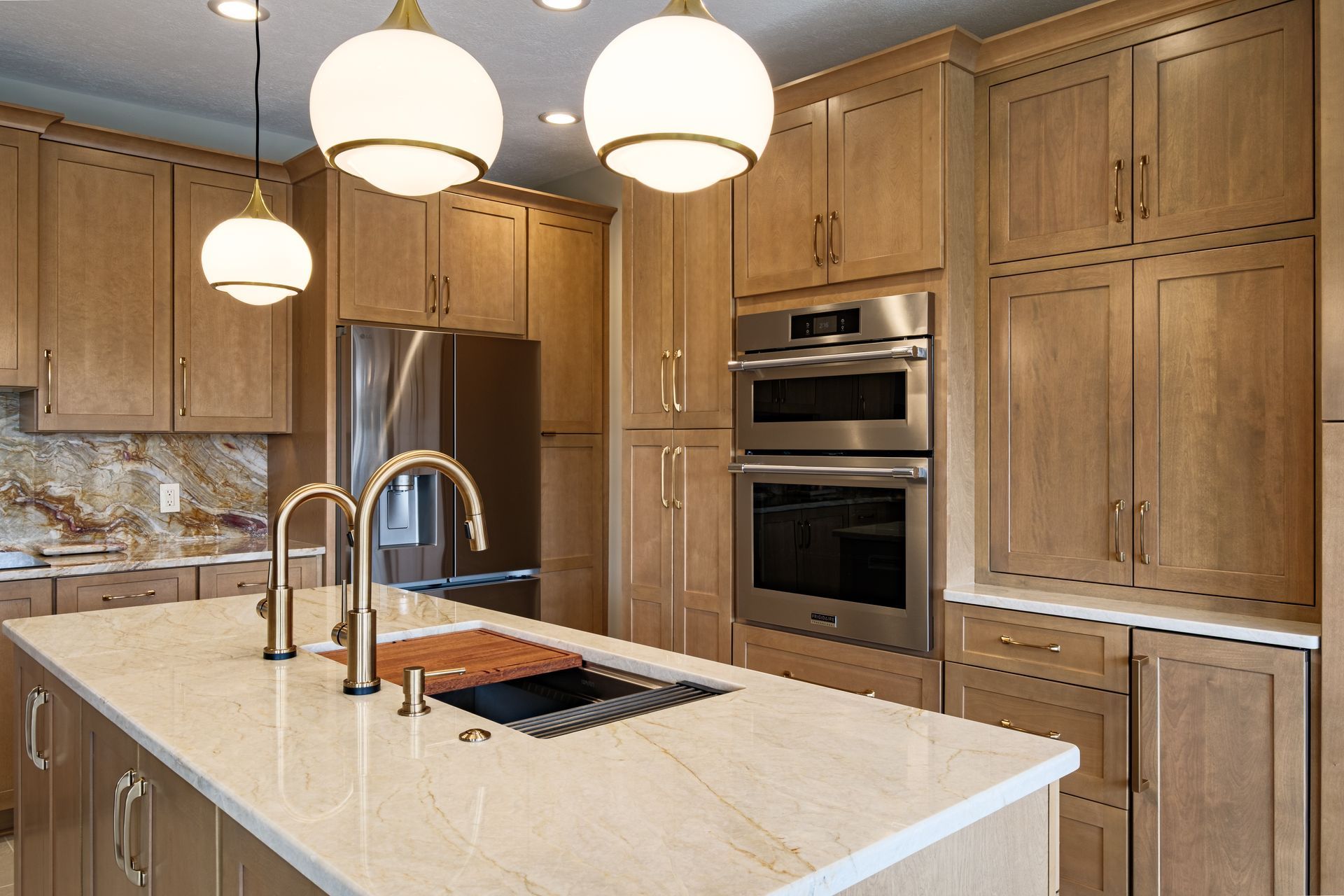 A modern kitchen with light wood cabinets, a large island, gold fixtures, and stainless steel appliances.