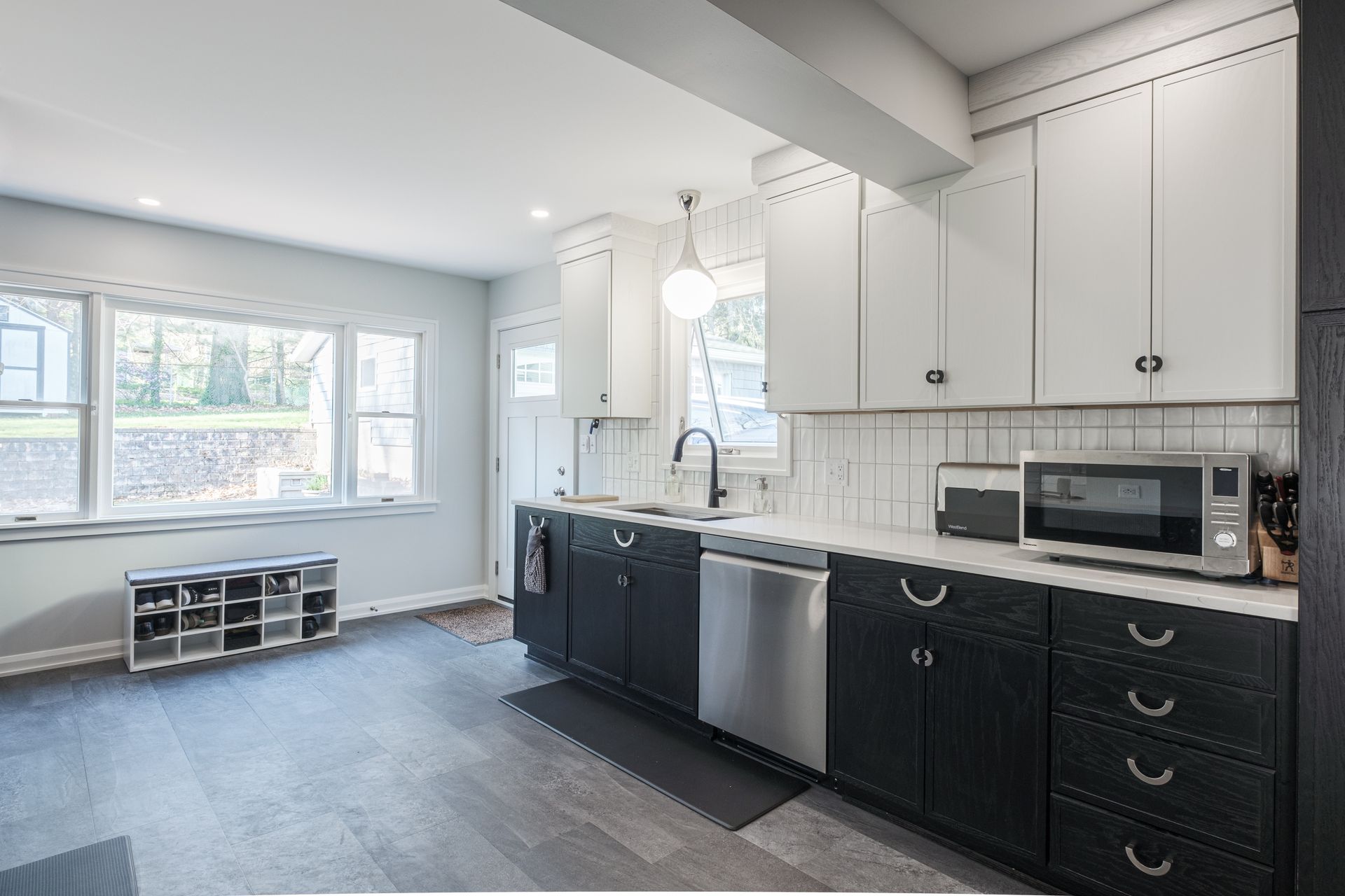 Modern kitchen with gray floors, white upper cabinets, dark lower cabinets, and stainless steel appliances.