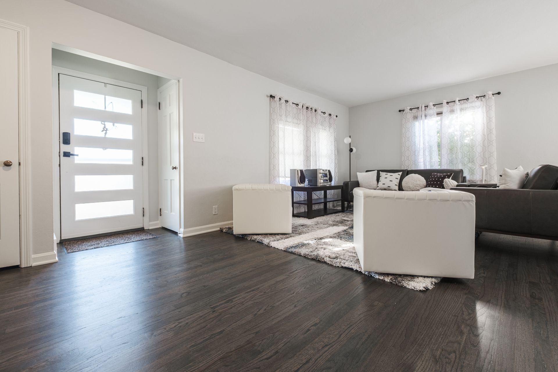 Modern living room with dark wood floors, white walls, and a light-filled entrance.