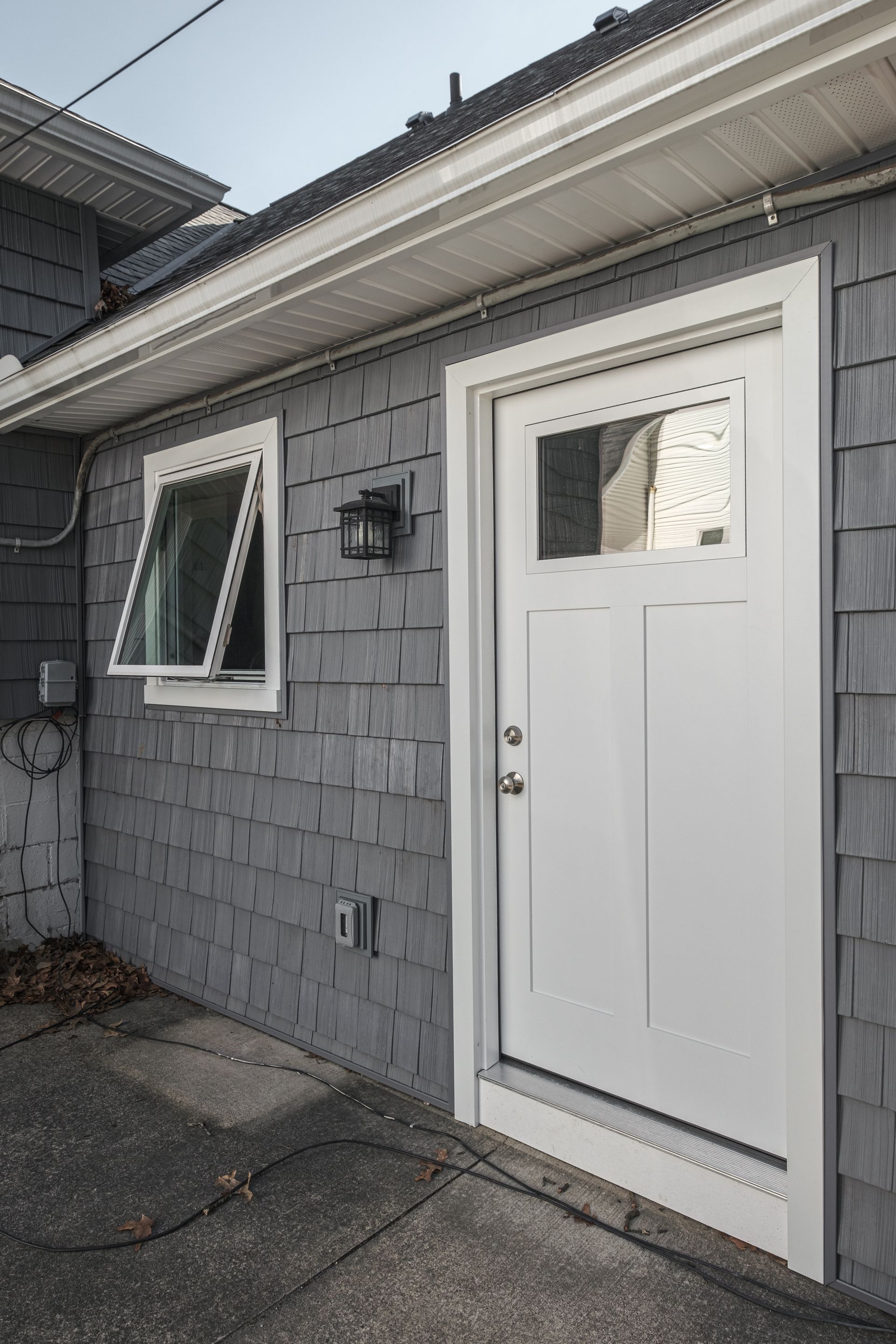 Gray shingled building exterior with a white door and open window.