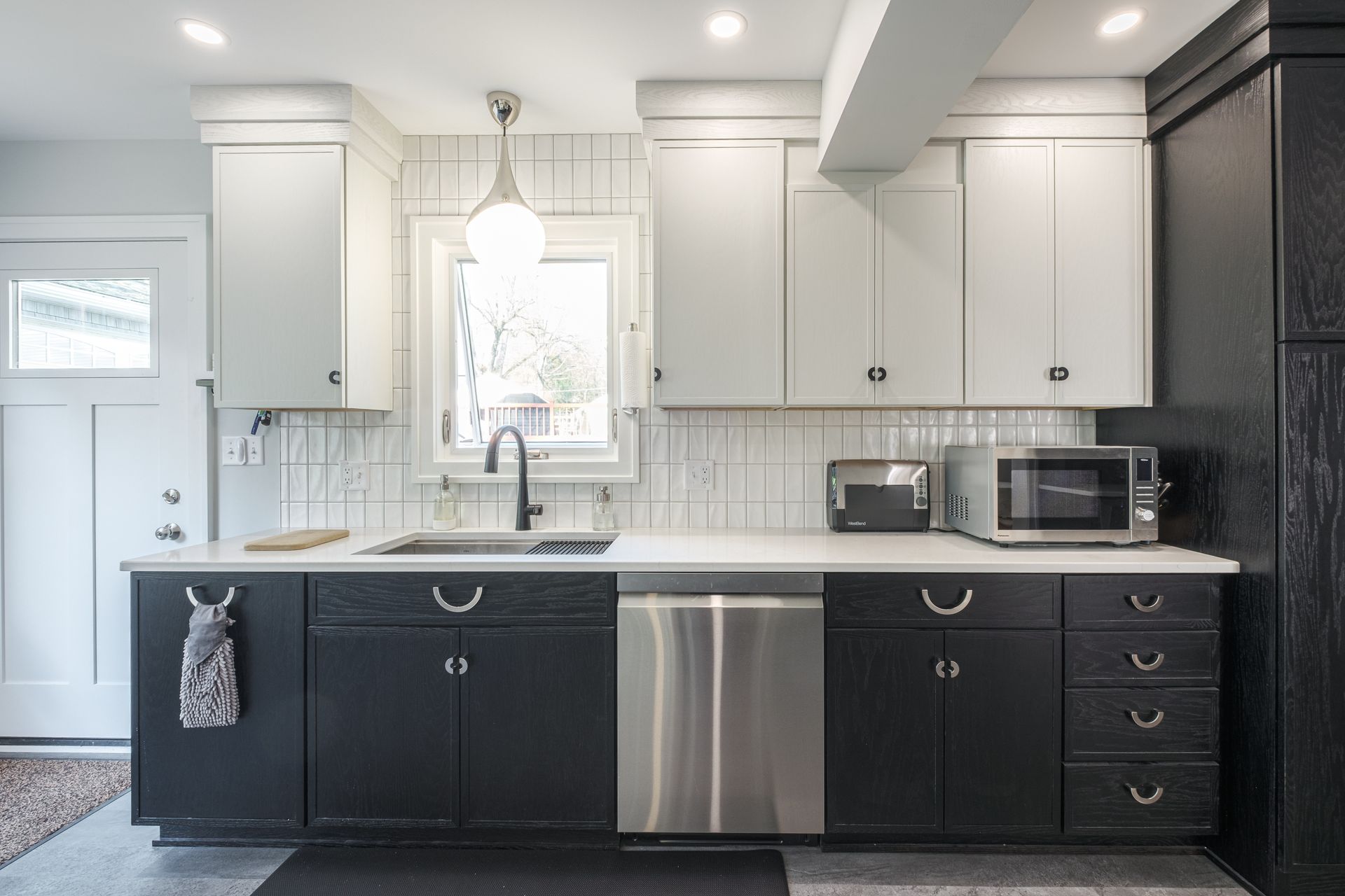 Modern kitchen with black and white cabinets, stainless steel appliances, and a window above the sink.