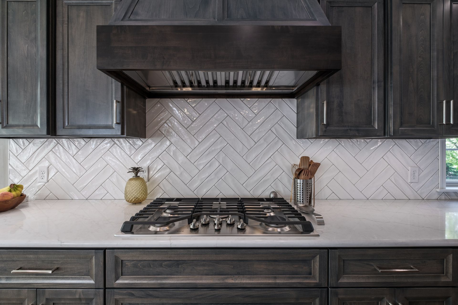 Gray kitchen with stovetop, white herringbone backsplash, and dark cabinets.
