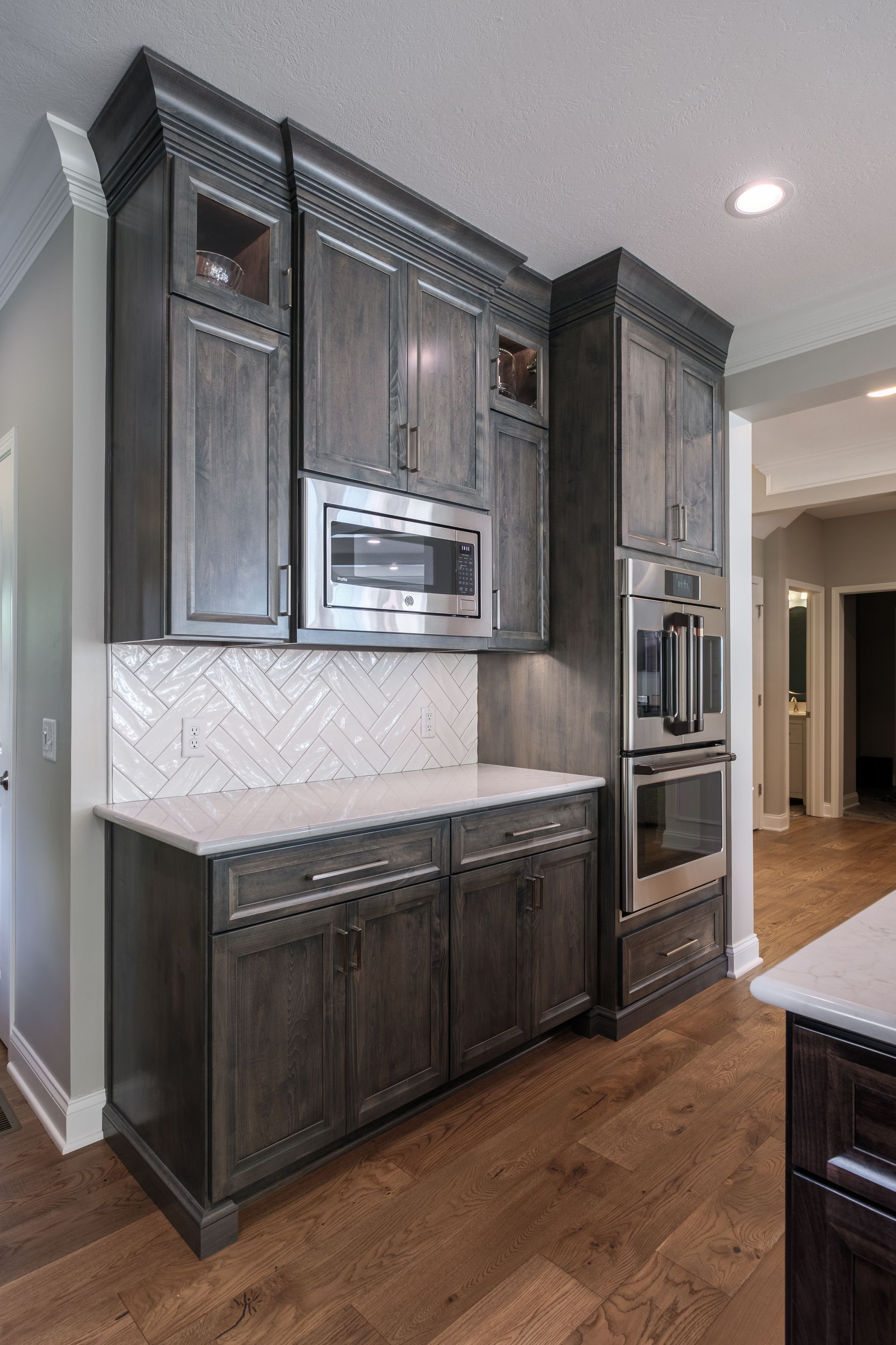Gray kitchen cabinets with built-in appliances and white backsplash. Wooden floor.