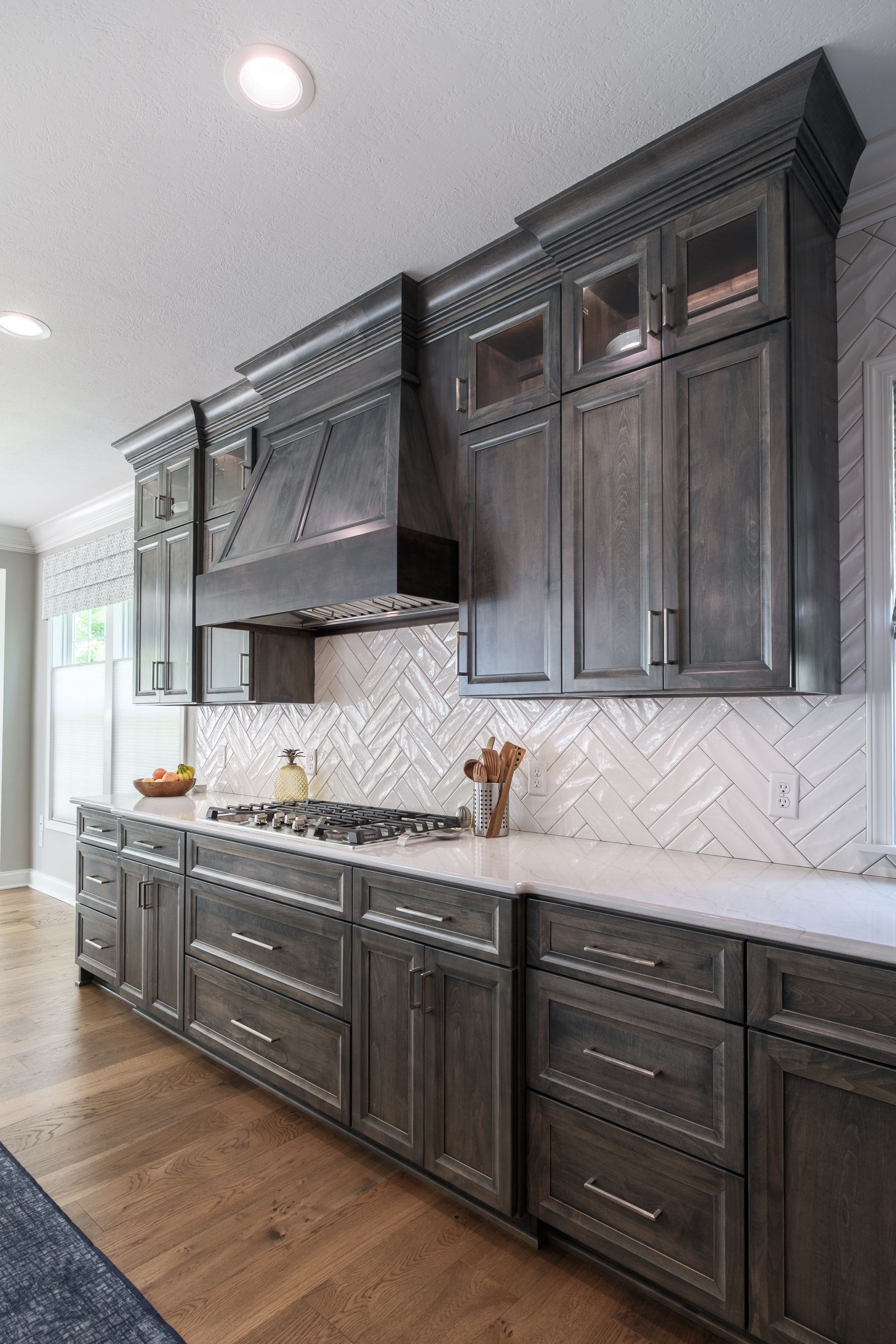 Gray kitchen cabinets with white countertops, herringbone backsplash, and wood floor.