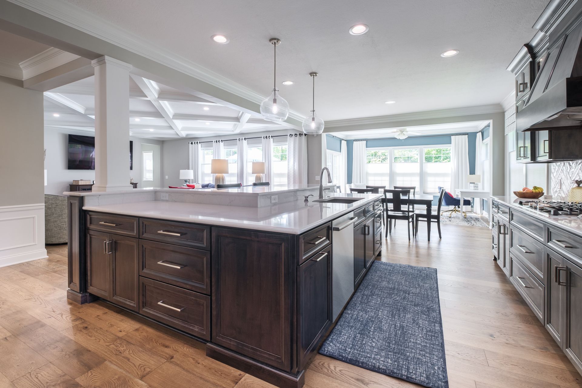 Modern kitchen with island, dark cabinets, light countertops, wood floor. View of dining area and living room.