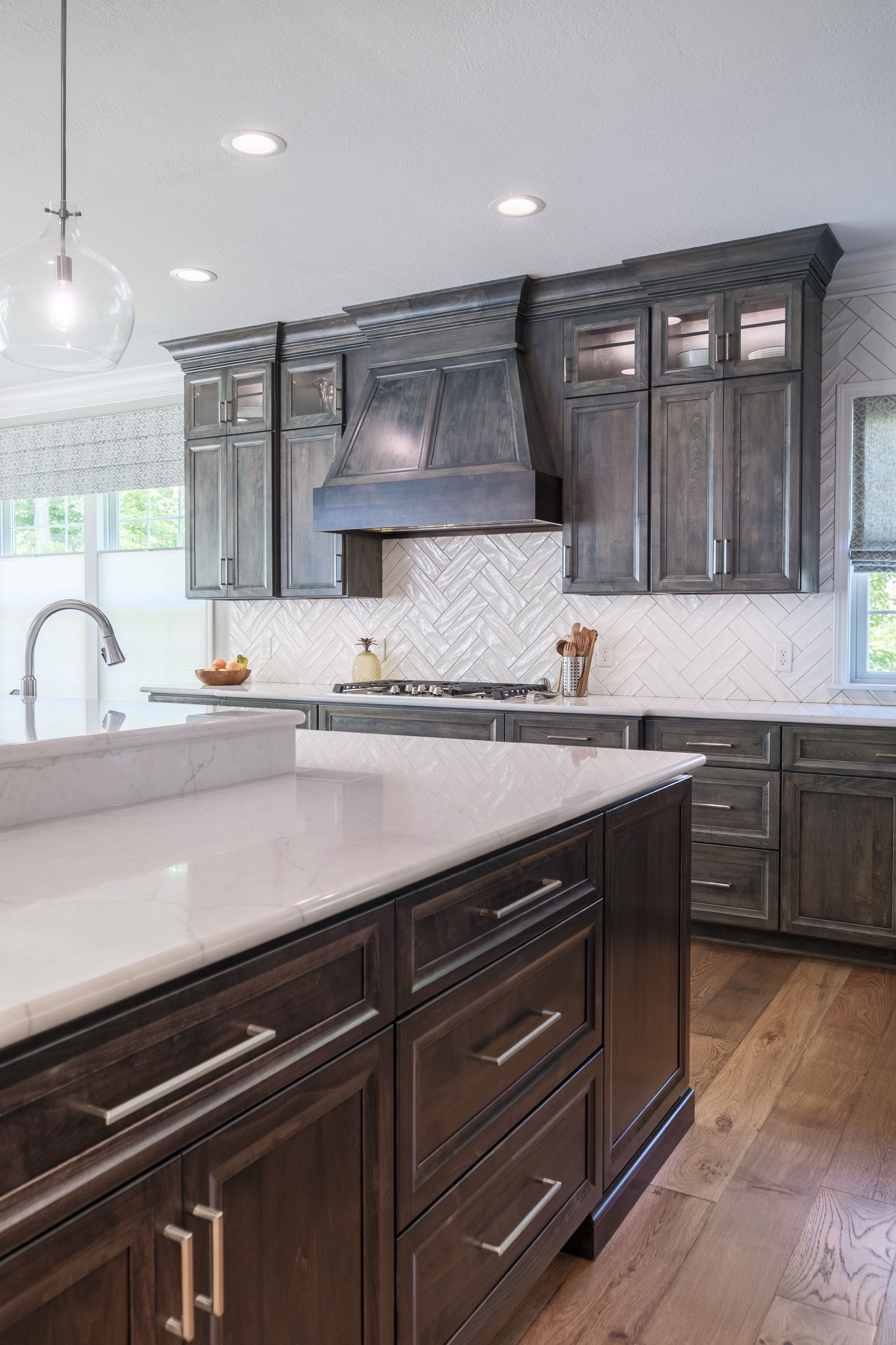 Gray kitchen with island, cabinets, white countertops, and herringbone backsplash.