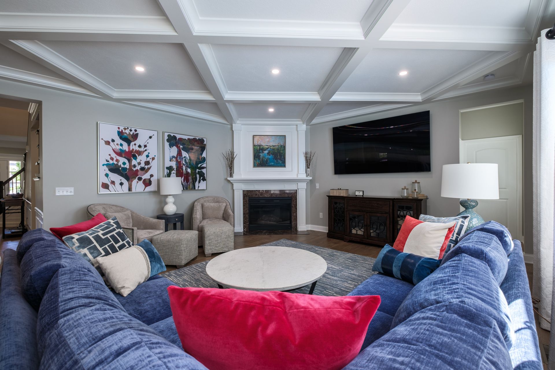 Cozy living room with a blue sectional sofa, fireplace, artwork, and coffered ceiling.