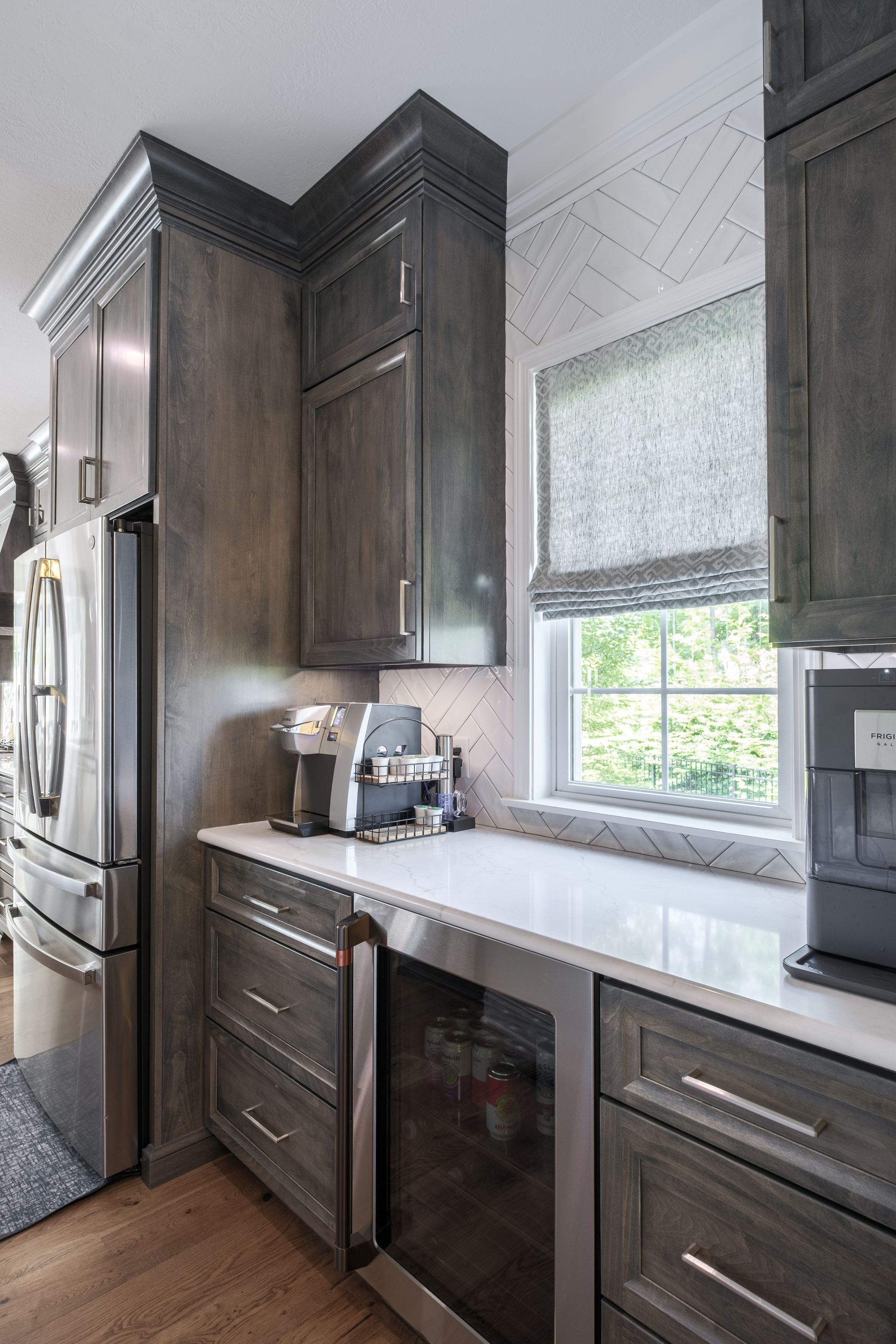 Kitchen corner with gray cabinets, white countertop, stainless steel appliances, and a window with a shade.