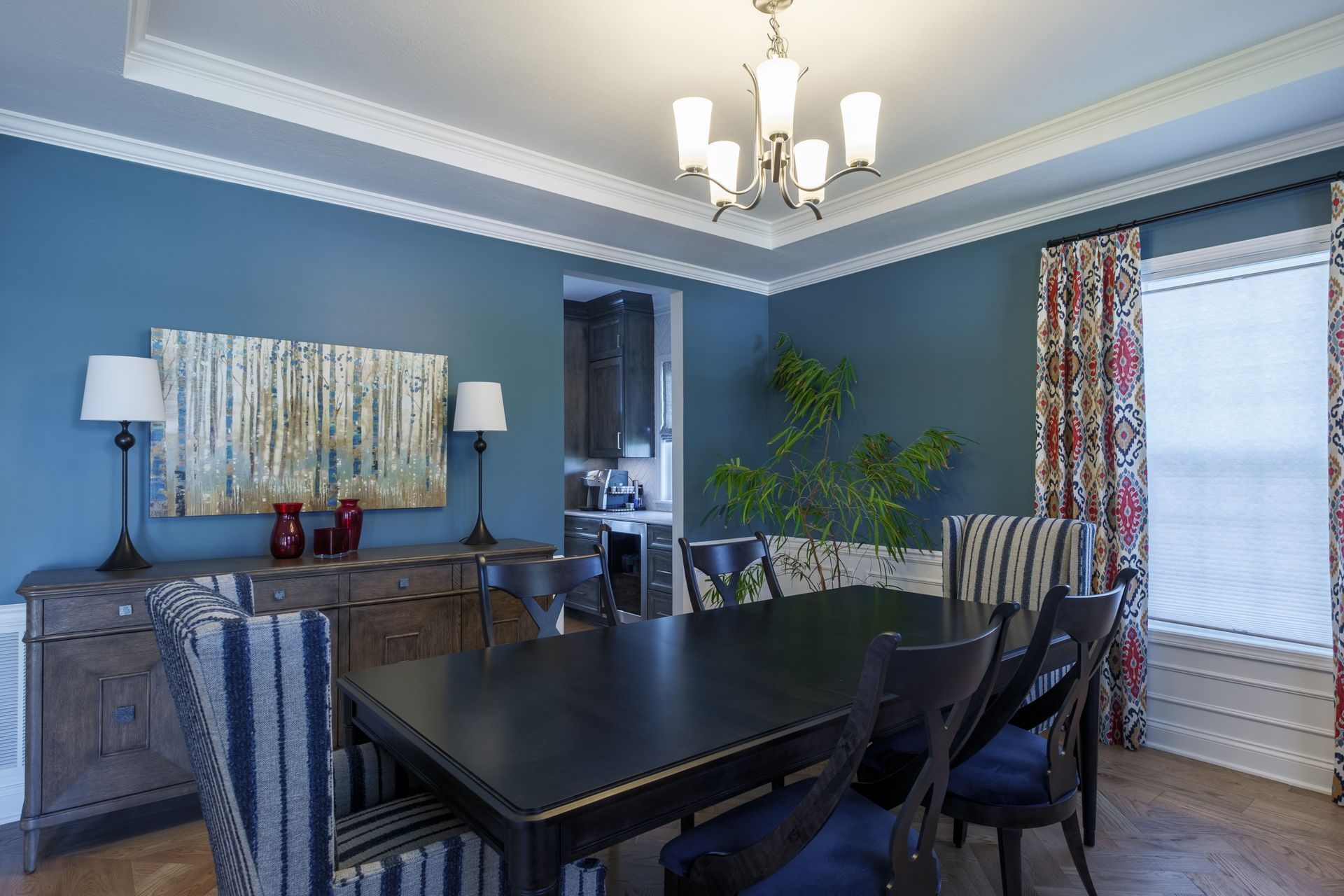 Dining room with a blue wall, black table, and striped chairs. Art and a buffet are also present.