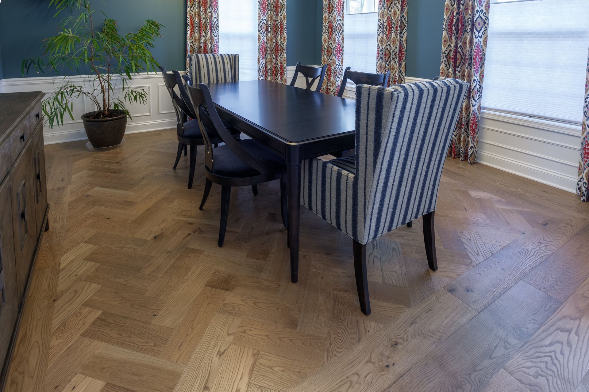 Dining room with dark table, patterned chairs, herringbone wood floor.