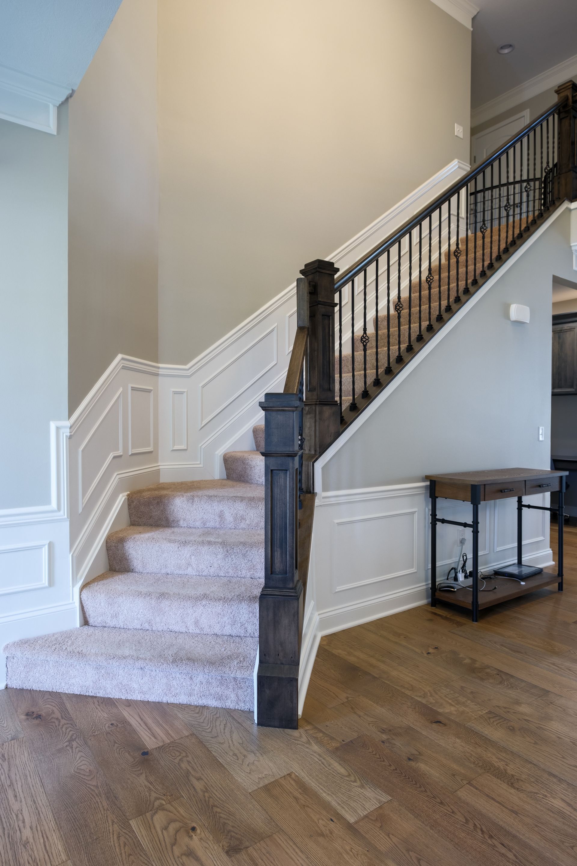Staircase with wooden floors, neutral walls, carpeted steps, dark railing, and a small table.