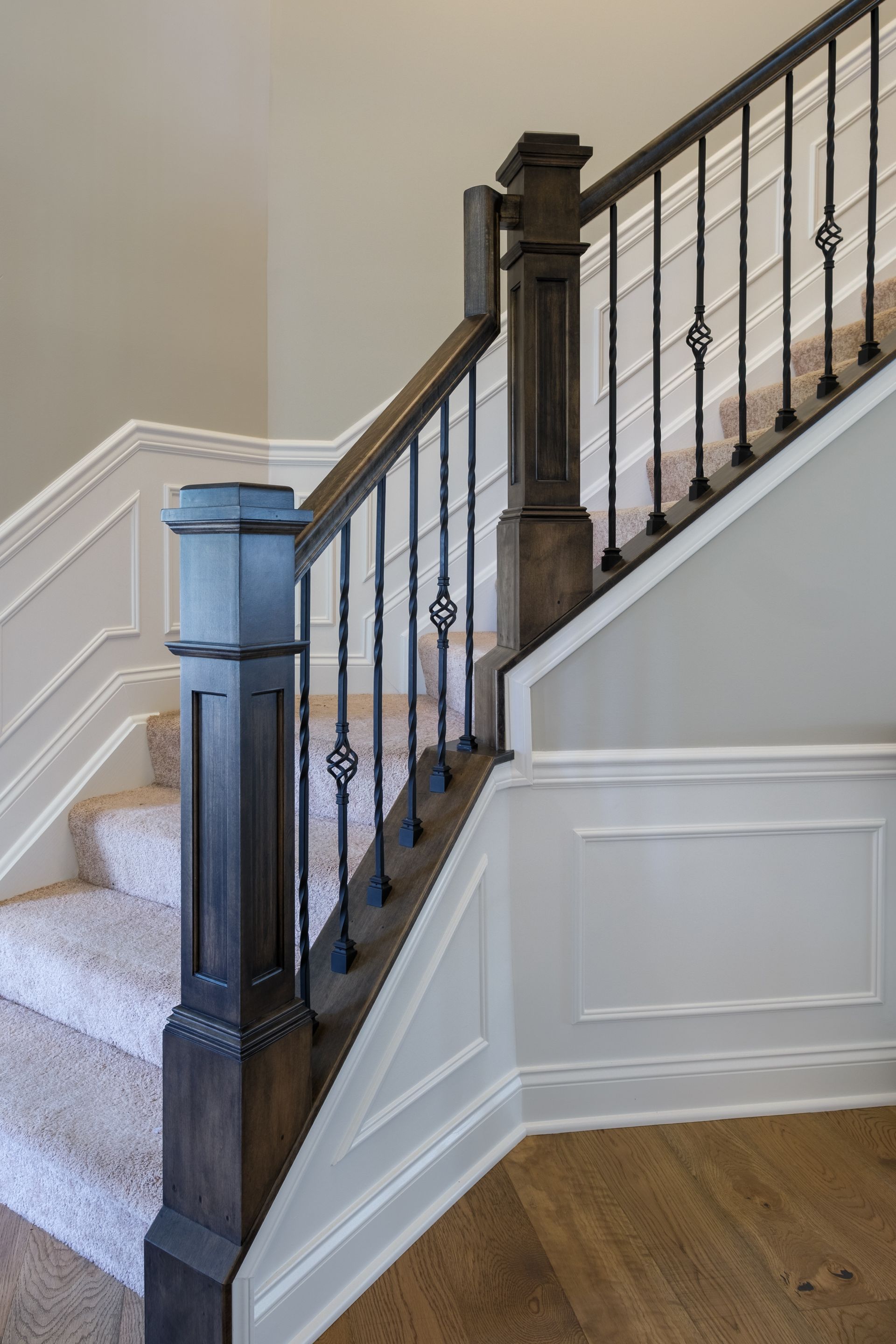 Staircase with dark wooden banister and wrought iron spindles. Carpeted stairs with white wainscoting.