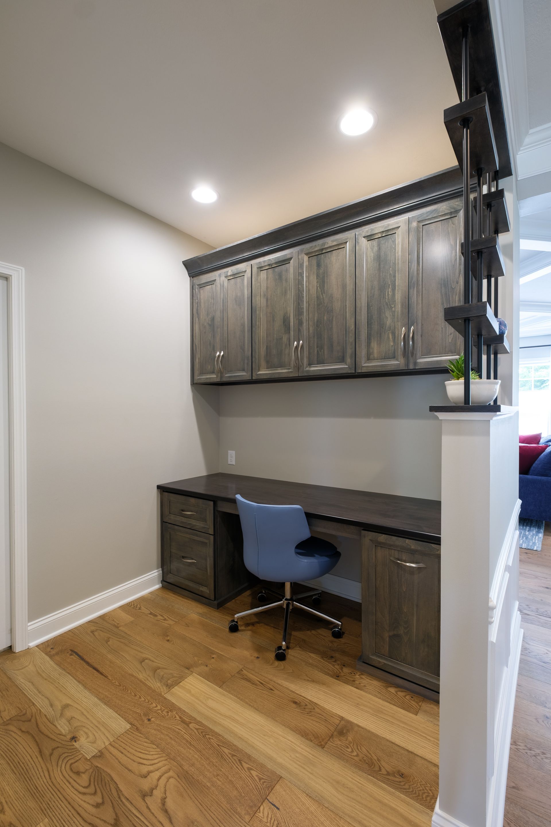 Built-in home office with gray cabinets and desk, blue chair, wood floor and wall, and partial open divider.