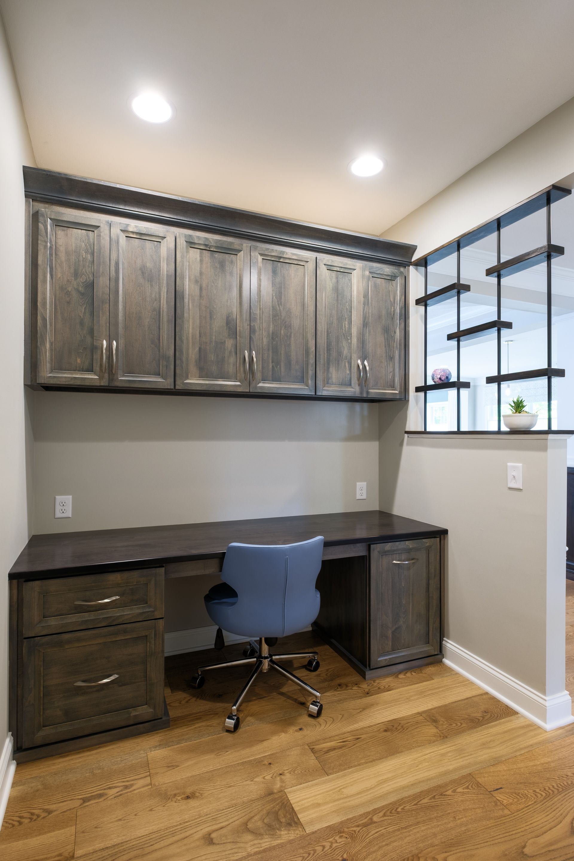 Built-in office with dark cabinets, desk, blue chair, and wood floor. Shelf wall is on the right.