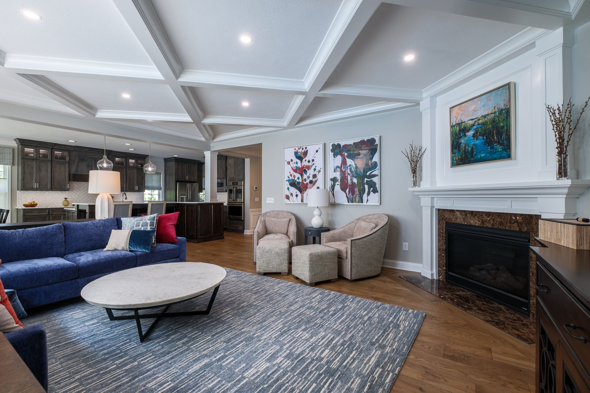 Living room with a blue sofa, fireplace, and open-concept kitchen. Gray walls and a coffered ceiling.