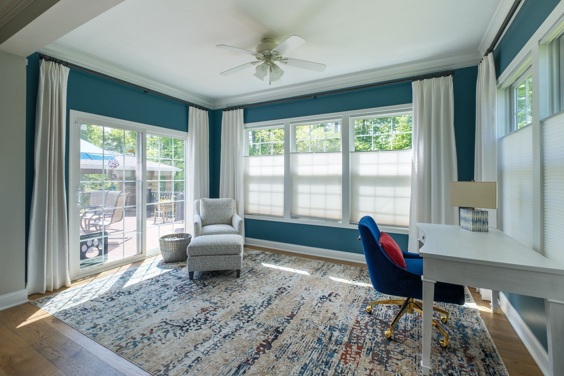 Bright home office with blue walls, white desk, and armchair next to patio door.