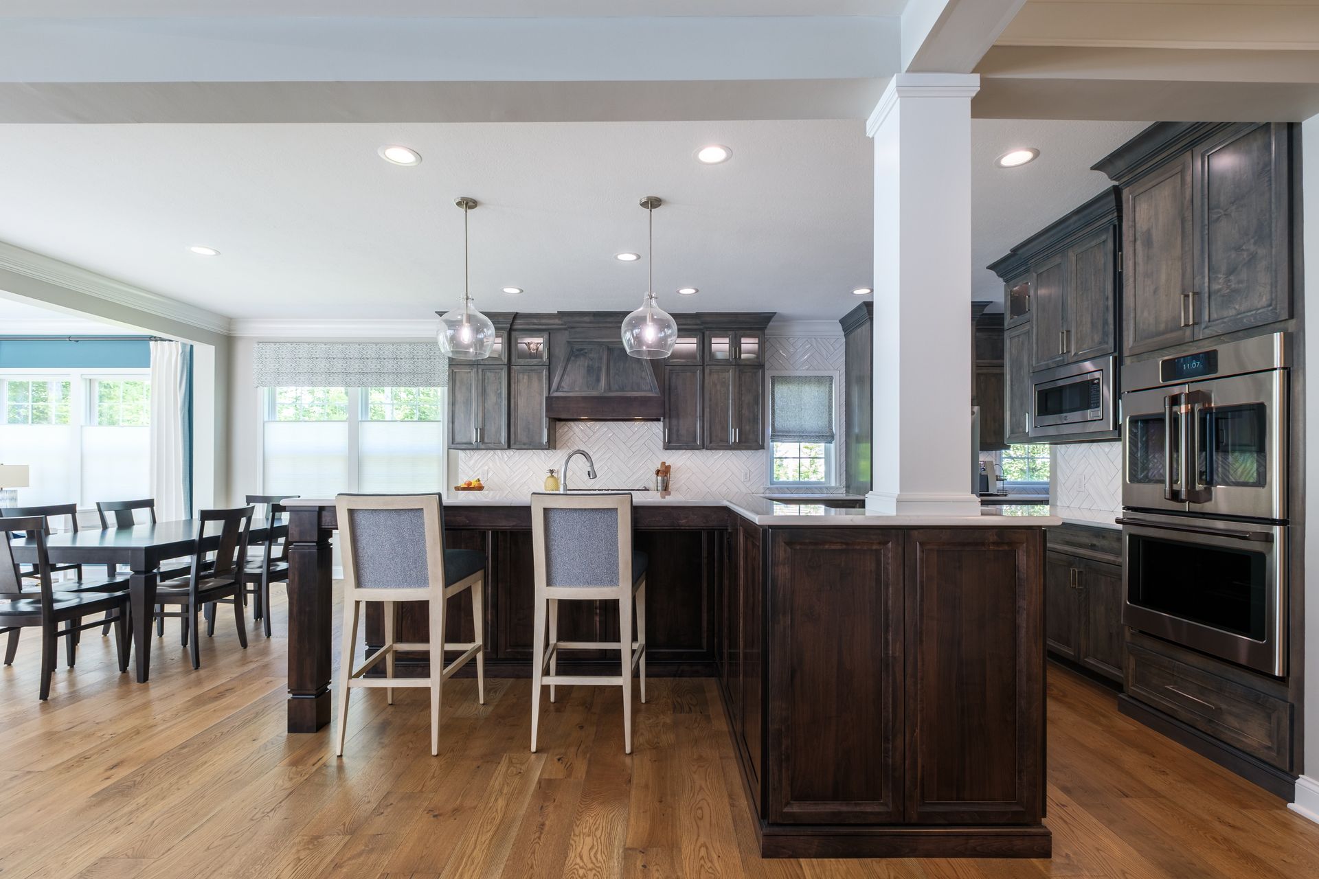 Open-concept kitchen with dark wood cabinetry, a white countertop island, and dining area with black table and chairs.