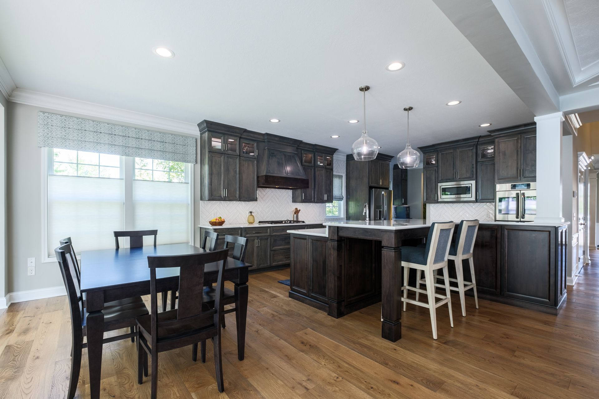 Modern kitchen with dark wood cabinets, island with stools, dining table, and hardwood floor.