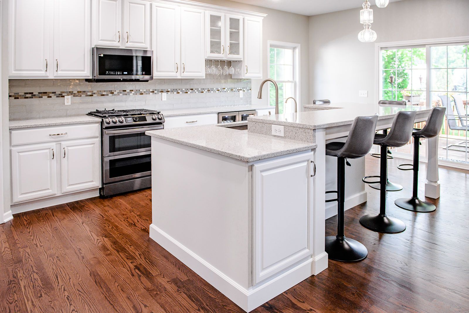 White kitchen with island, stainless steel appliances, dark wood floors, and grey bar stools.