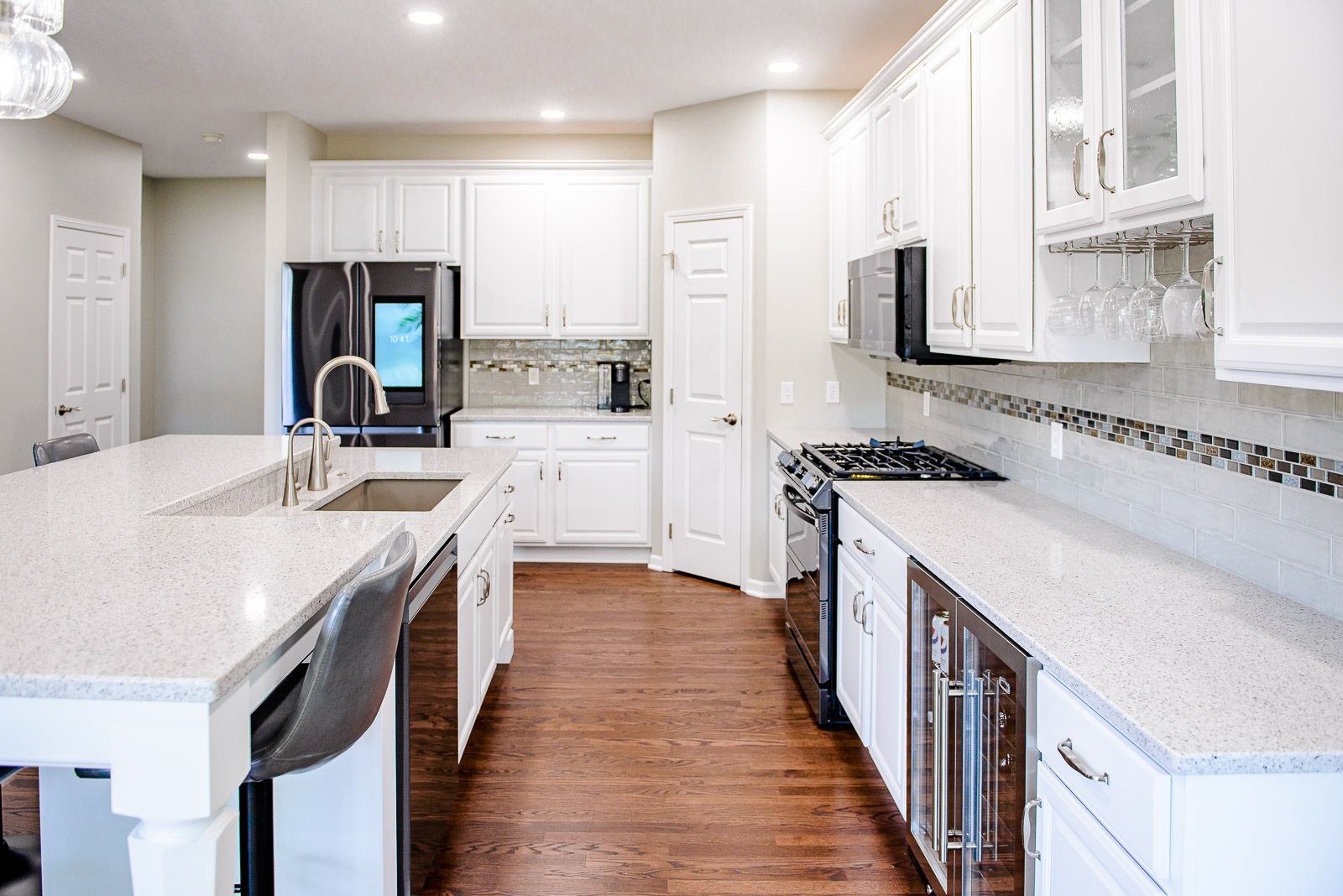Bright white kitchen with large island, stainless steel appliances, and wood floors.