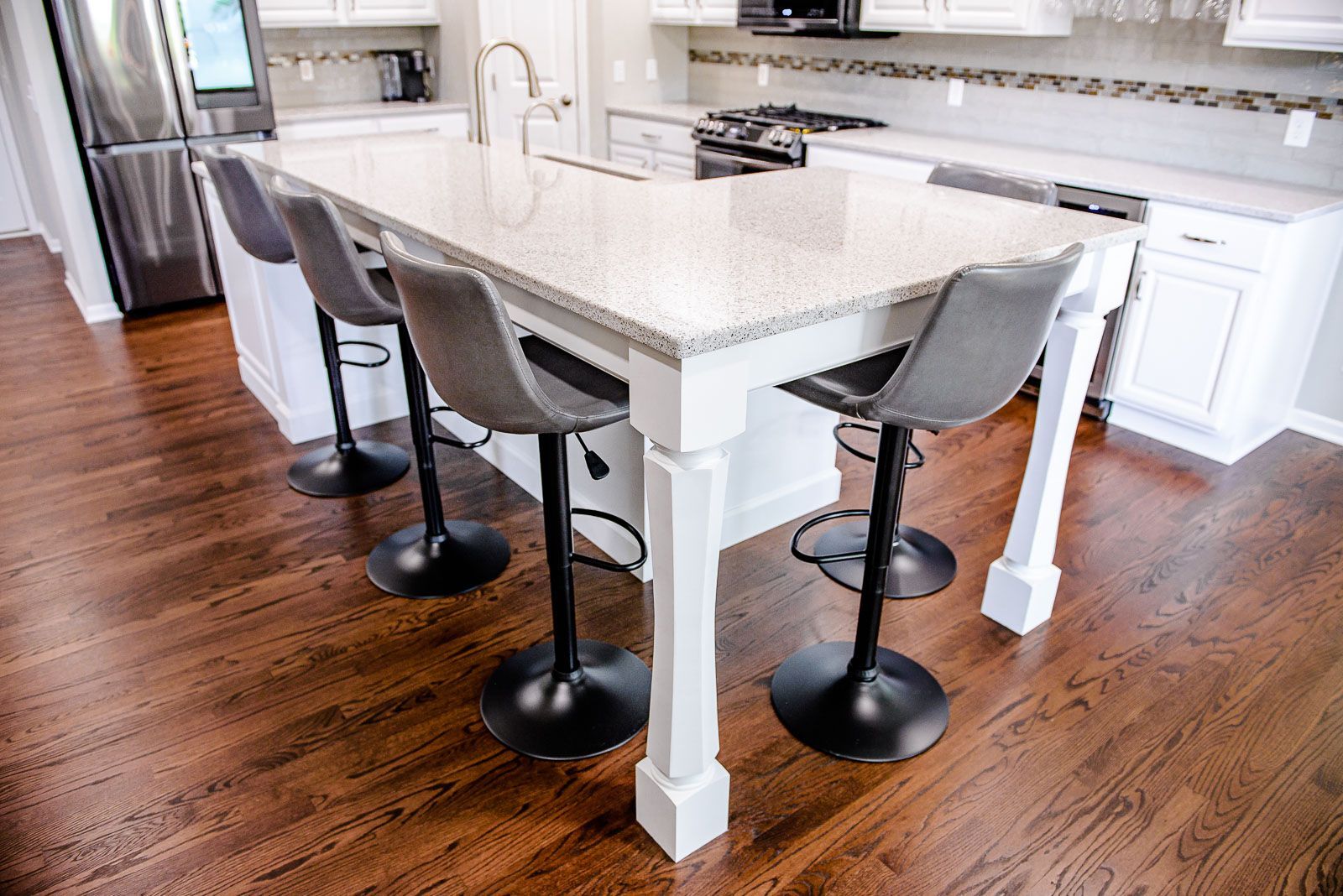 Kitchen island with gray stools, granite countertop, and dark wood floor.