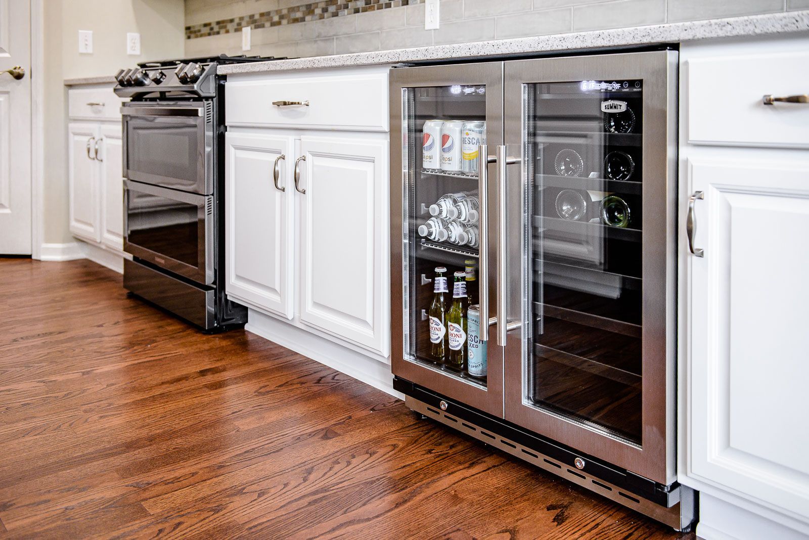 Built-in beverage cooler in a kitchen, next to white cabinets and a stove, with hardwood floors.