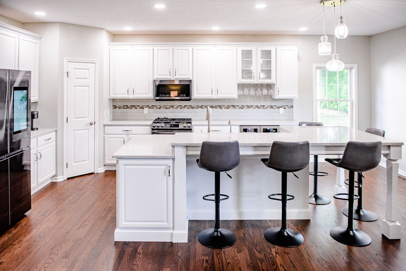 White kitchen with island and bar stools, dark wood floors, stainless steel appliances, and a door to the outdoors.