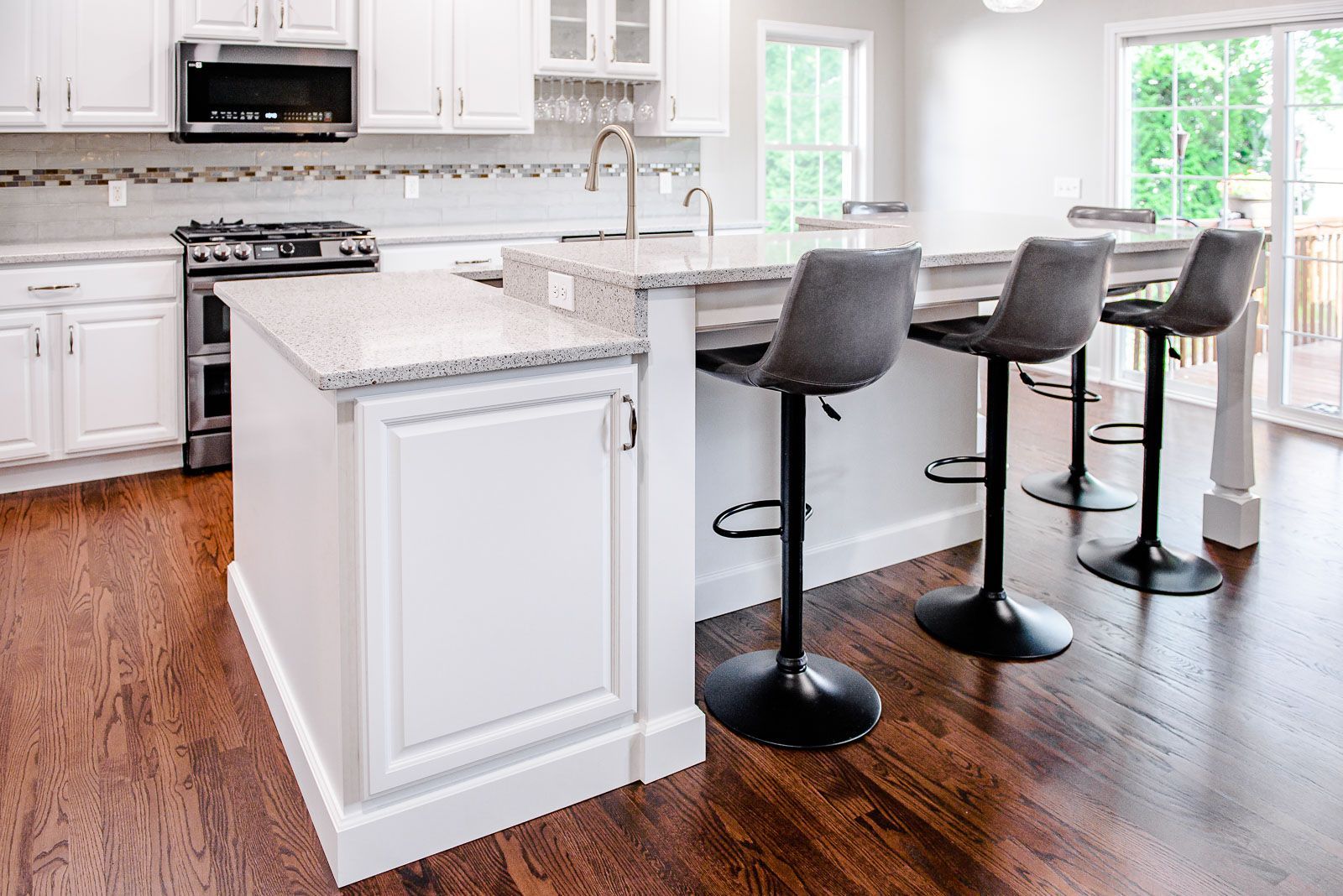 Modern kitchen with white cabinets, island with stools, and dark wood floors.