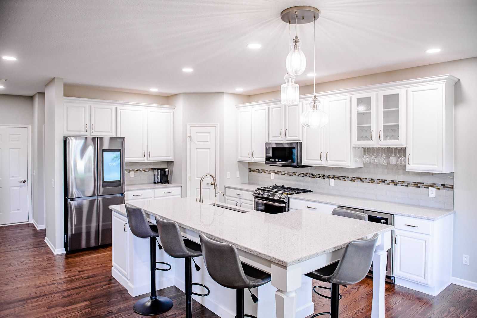Bright white modern kitchen with island, stainless steel appliances, and dark wood floors.