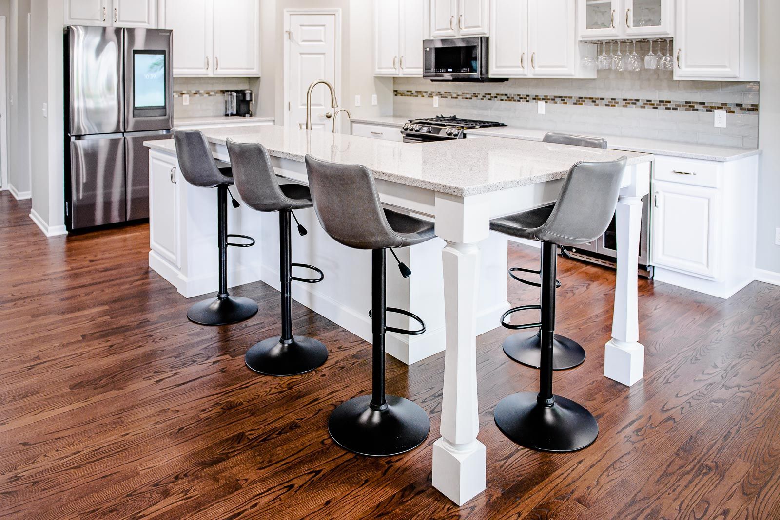 Modern kitchen with island and bar stools, stainless steel fridge, and wooden floors.