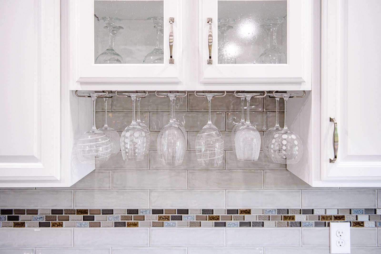 White kitchen cabinets with stemware hanging below; a tiled backsplash is visible.