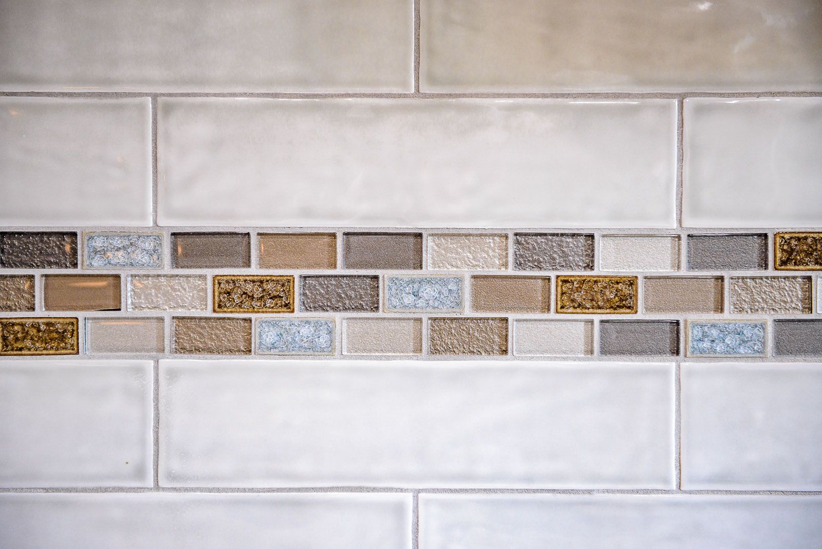 Cream-colored tile wall with a decorative mosaic strip of various colored and textured tiles.