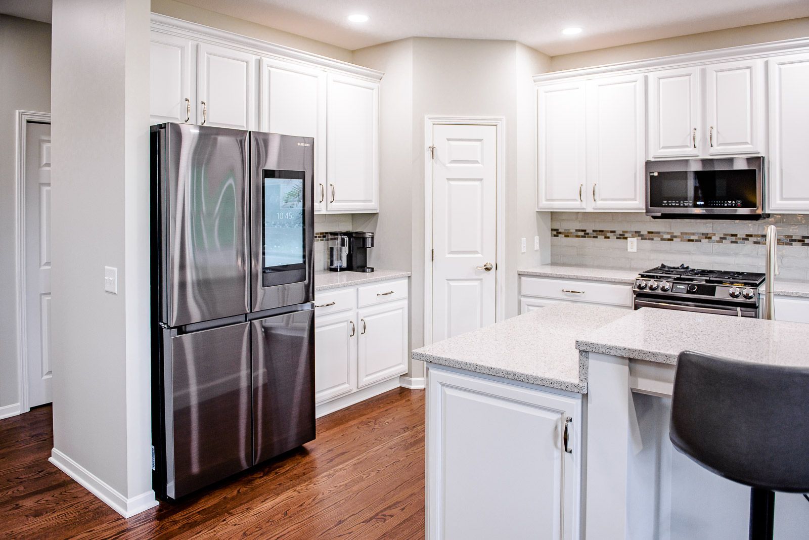 White kitchen with stainless steel refrigerator and wood floors.