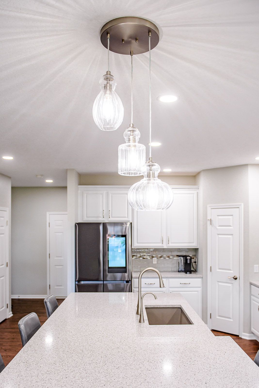 Kitchen with white cabinets, island with sink, and three pendant lights.