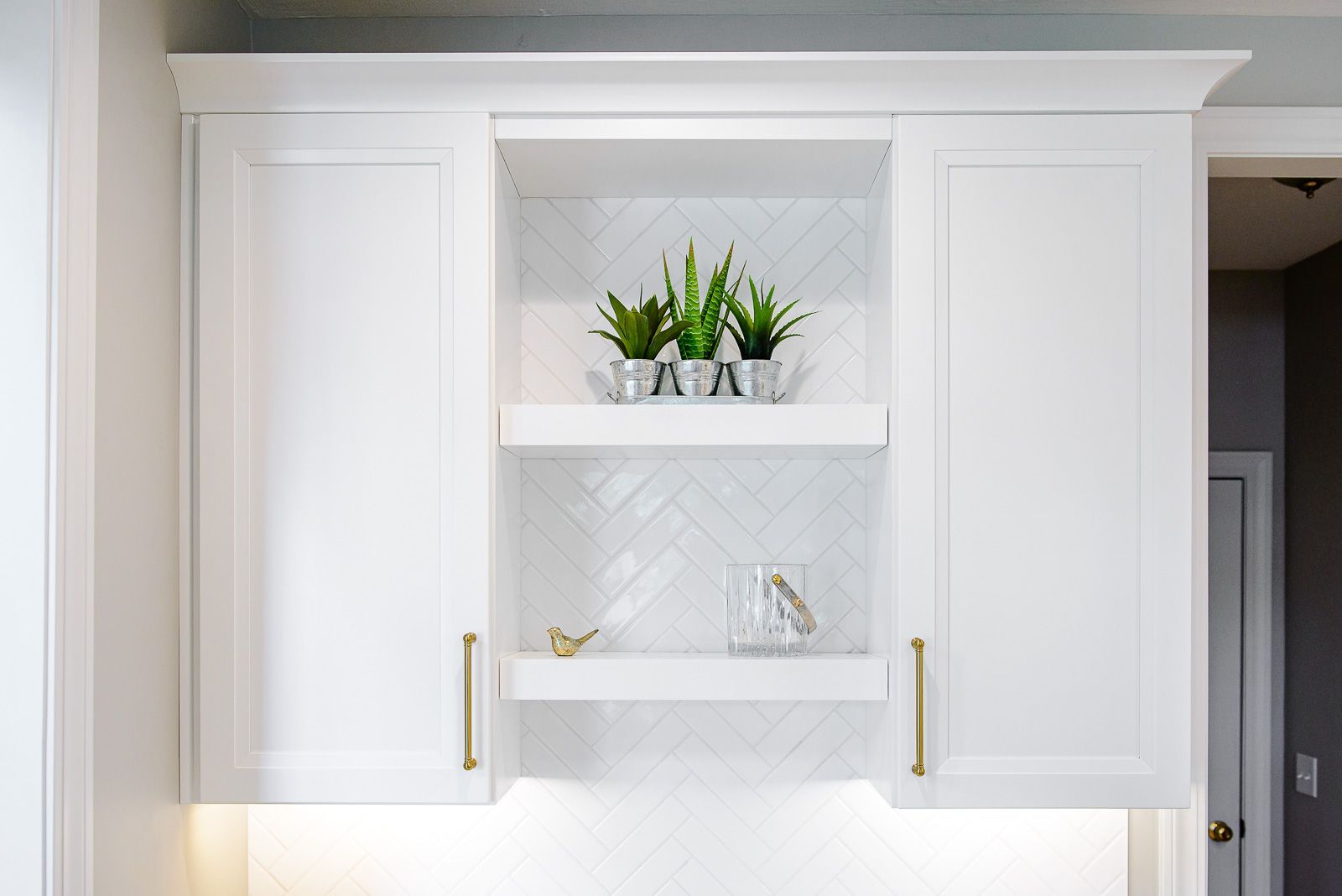 A kitchen with white cabinets and a shelf with a plant on it.