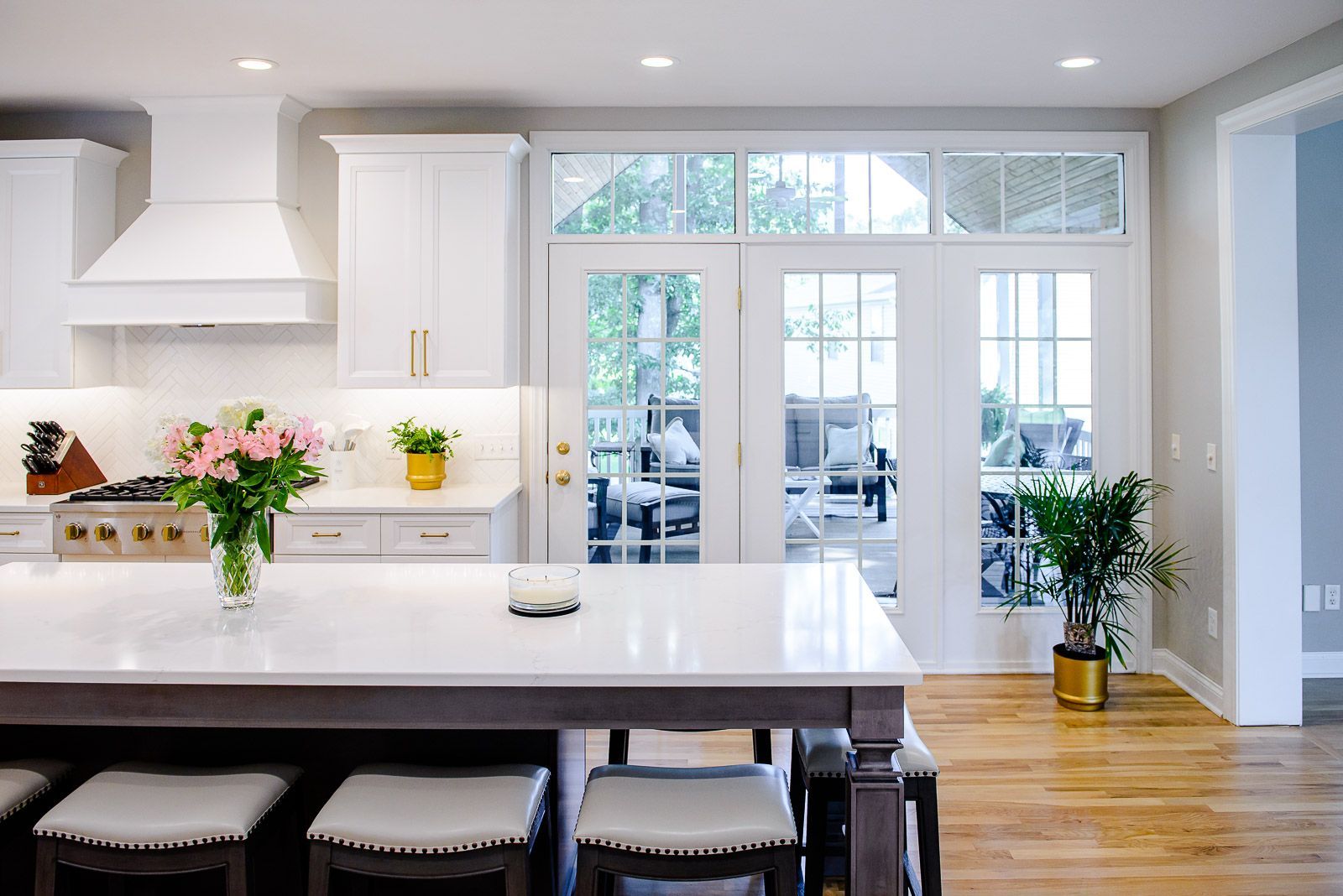 A kitchen with white cabinets , a large island , stools , and french doors.