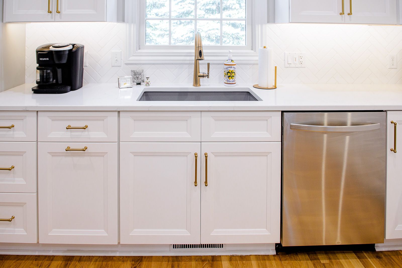 A kitchen with white cabinets , a sink , and a stainless steel dishwasher.