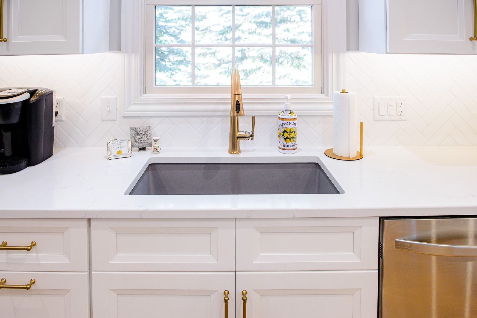A kitchen with white cabinets , stainless steel appliances , a sink , and a window.