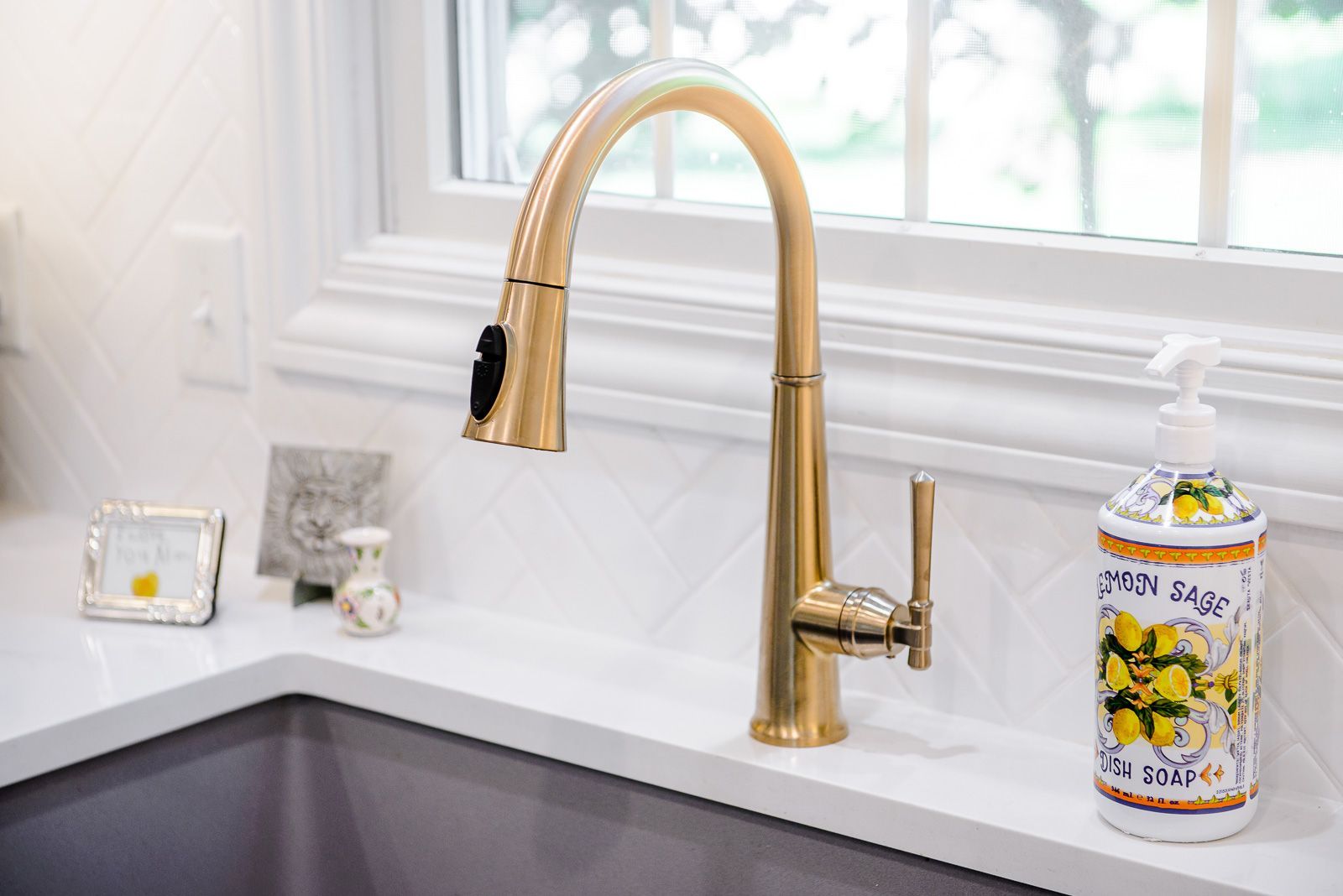 A kitchen sink with a gold faucet and a soap dispenser on the counter.