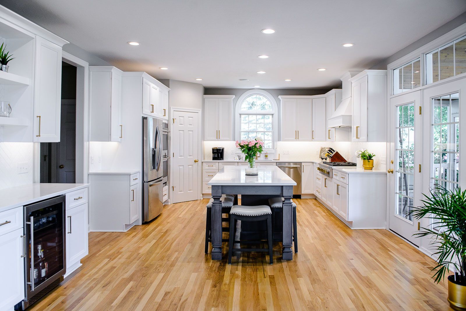 A kitchen with white cabinets , stainless steel appliances , hardwood floors and a large island.